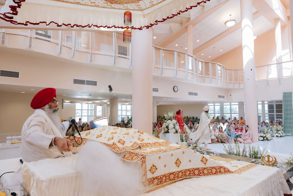 Wide Anand Karaj view with Guru Granth Sahib in the foreground, officiant, couple, congregation and the Sikh Institute Fresno hall architecture