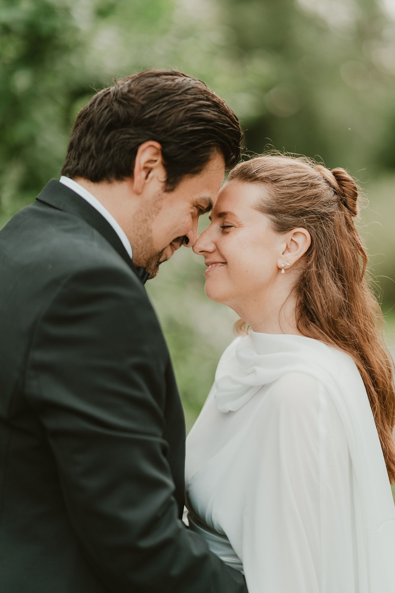 A wedding couple lean their foreheads together outdoors