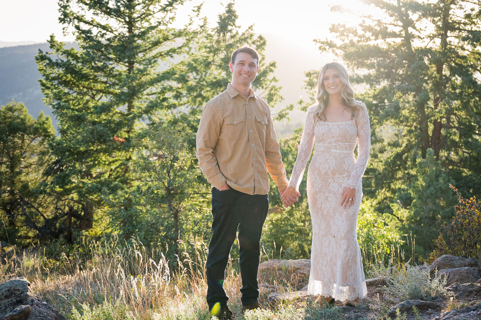 Engaged couple on a Colorado mountain overlook in a long ivory lace dress and a camel button down