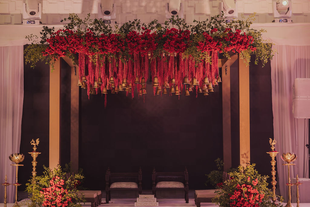 Full-width wedding mandap with red flowers, hanging bells, gold columns and a black backdrop at Regency Event Center in Clovis