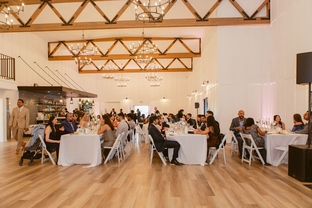 Wide indoor Evanelle Vineyards reception showing timber trusses, chandeliers, long dining tables, bar, dance floor and seated guests