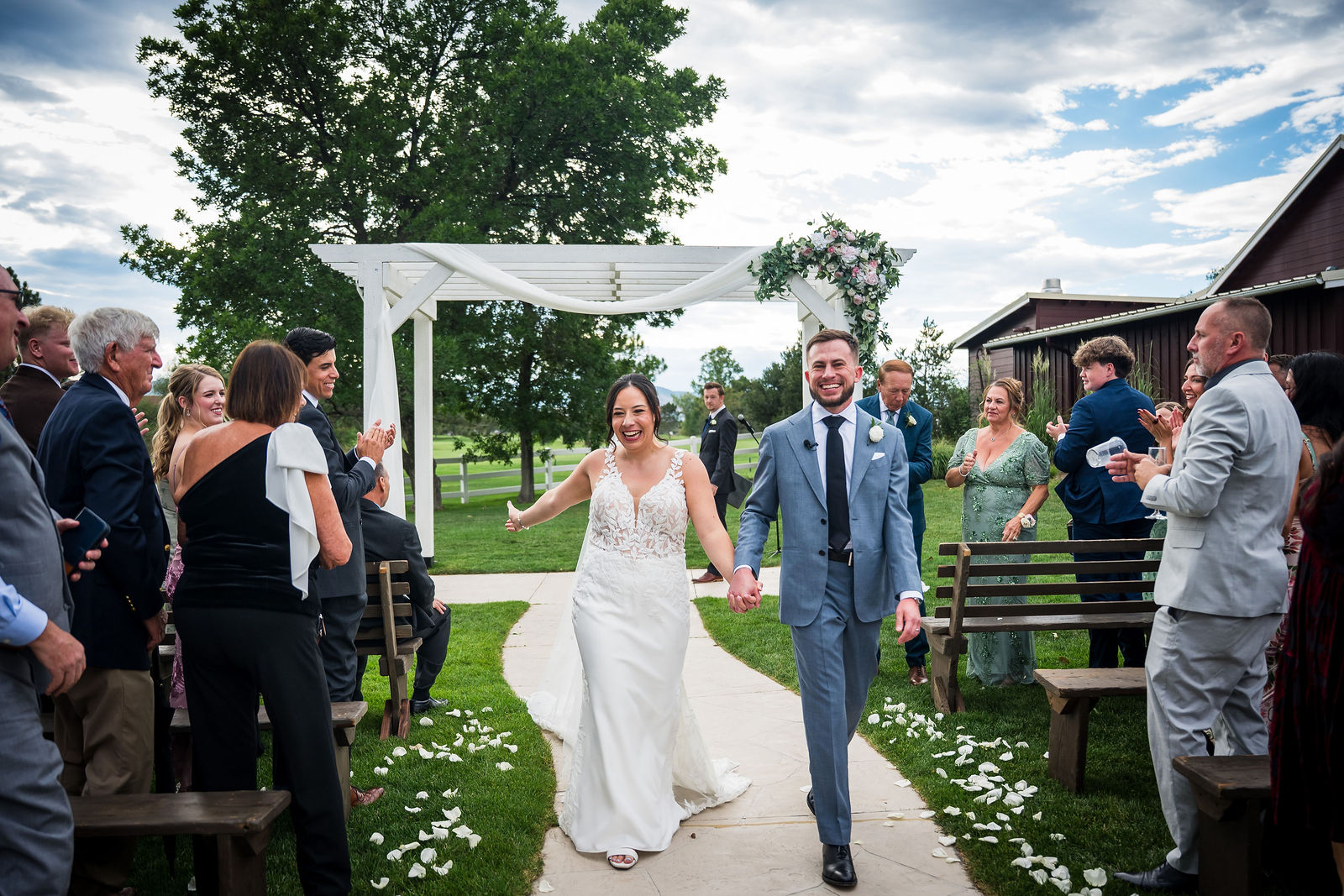 Bride and groom walking back up the aisle after their ceremony beside the red barn at The Barn at Raccoon Creek in Littleton Colorado