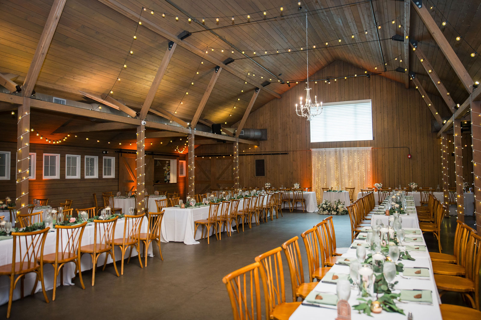 Long reception tables set under market lights inside the historic barn at The Barn at Raccoon Creek in Littleton Colorado