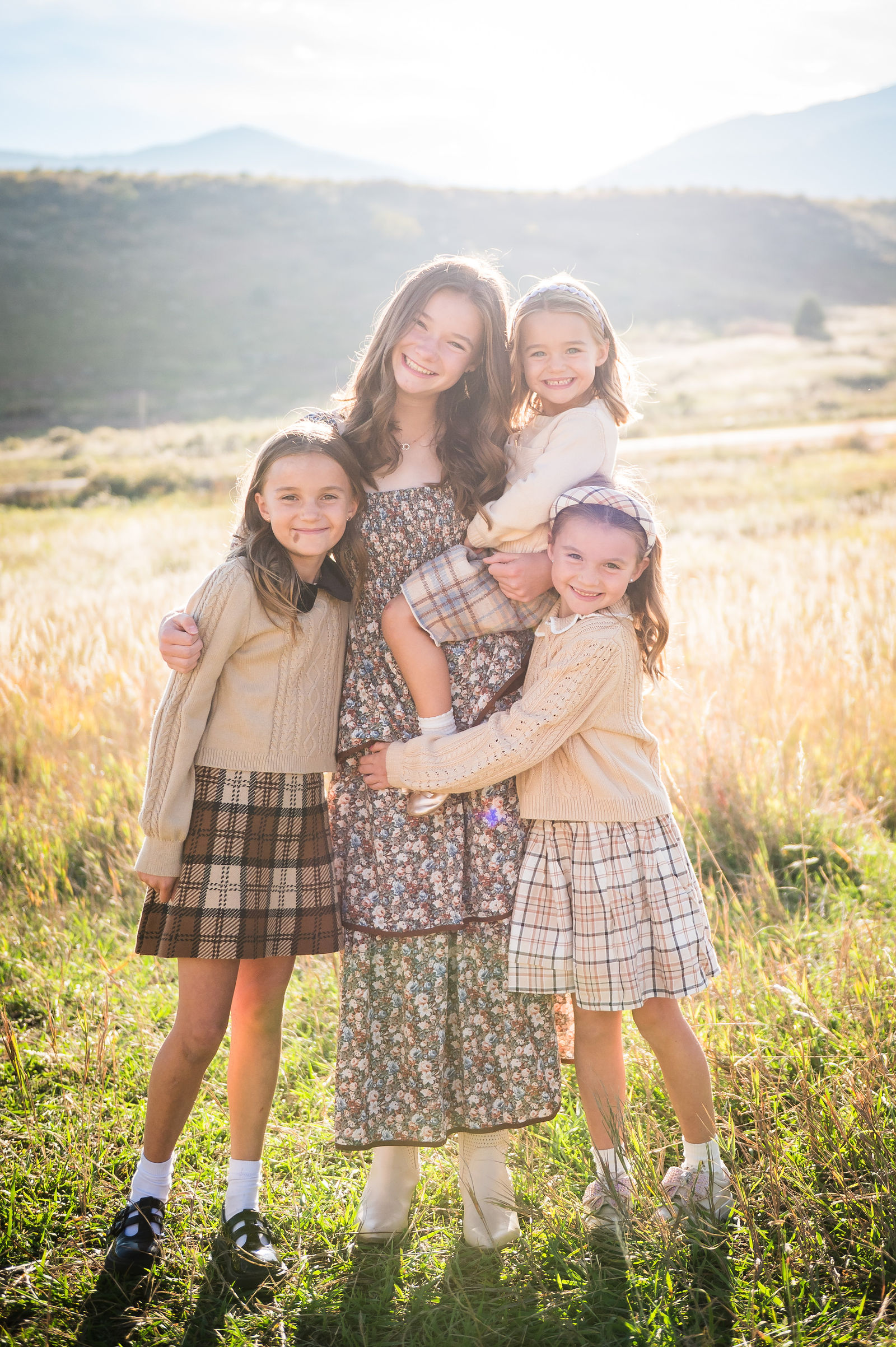 Three sisters in cream sweaters and plaid skirts at golden hour in the Colorado foothills