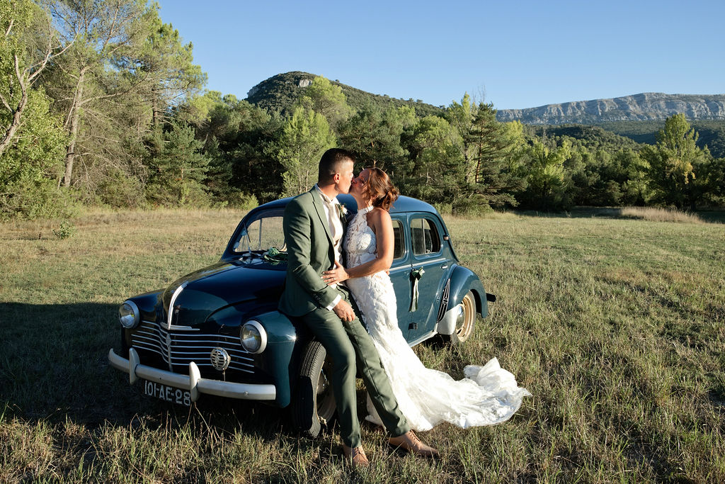 Audrey et Sébastien s’embrassent près de la voiture ancienne bleue, devant les collines.