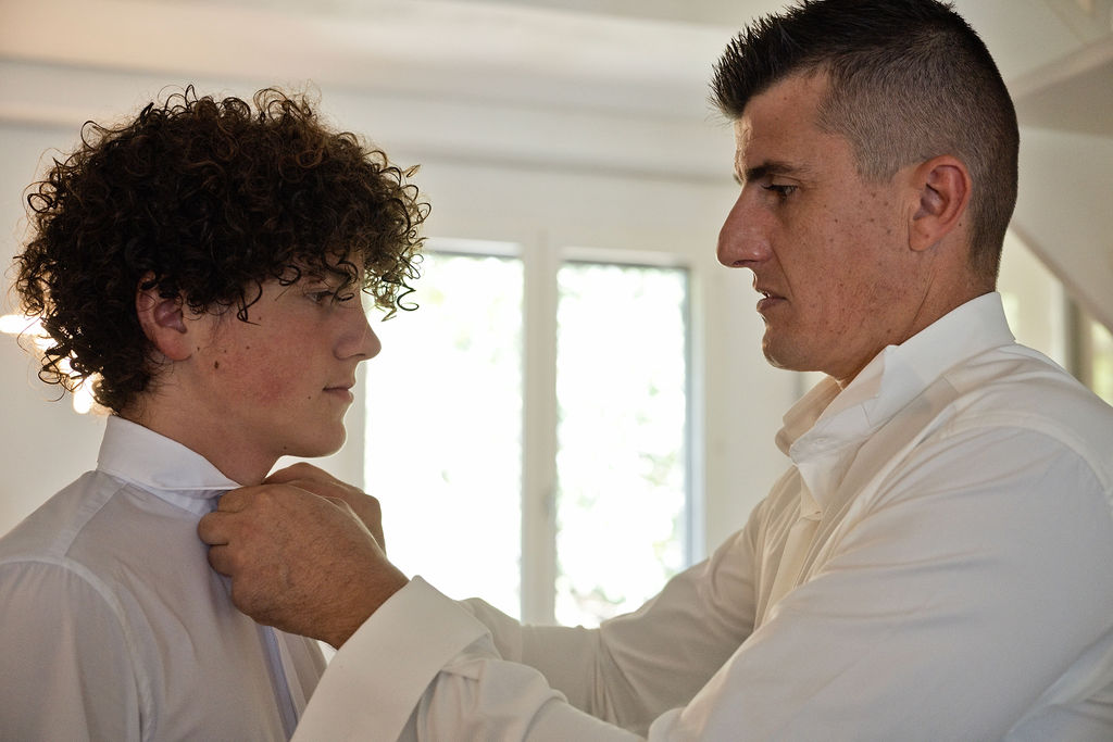 Sébastien ajuste le col de chemise d’un jeune proche pendant les préparatifs.