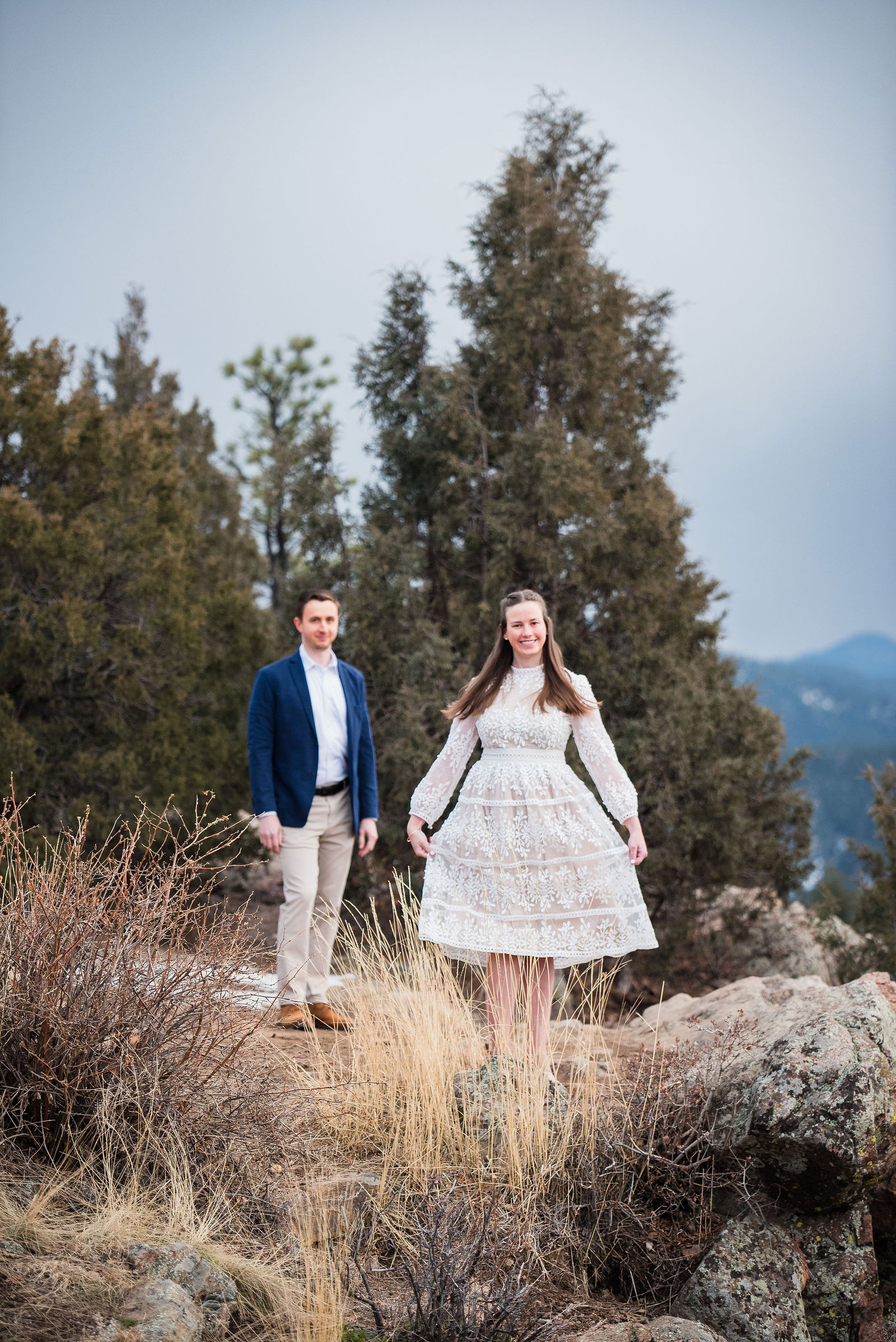 Engaged couple in a navy blazer and khakis with a long cream lace dress in the Colorado snow