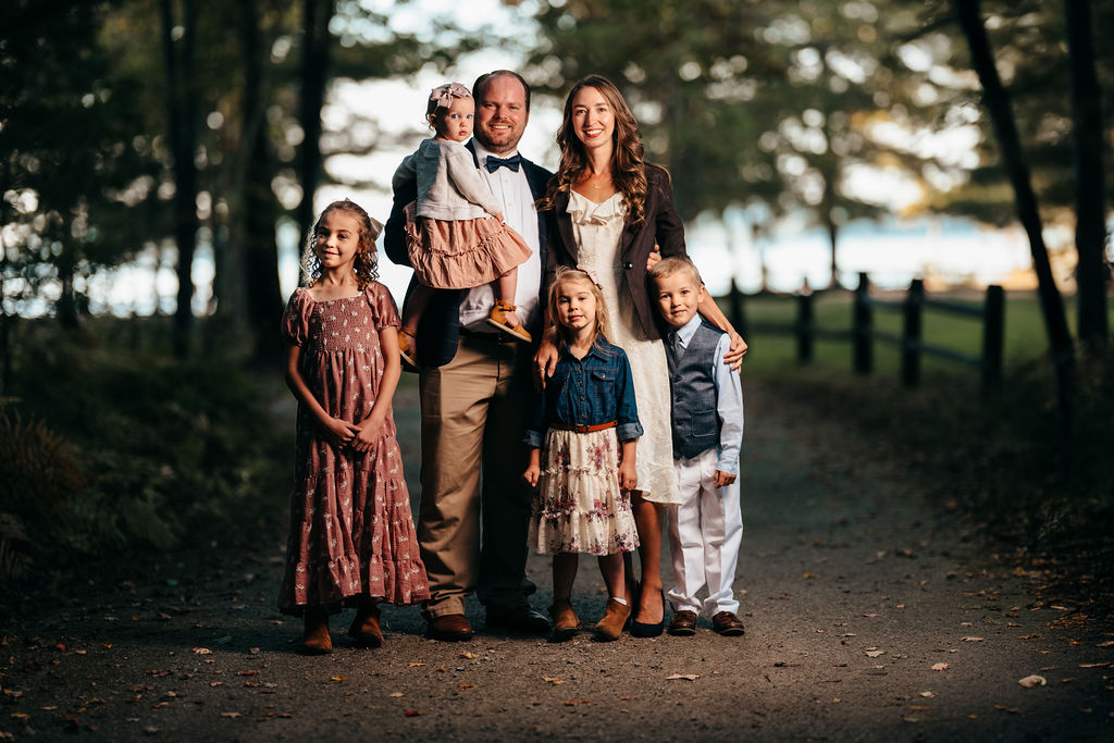 Haynes family of six posed together on a wooded path at dusk