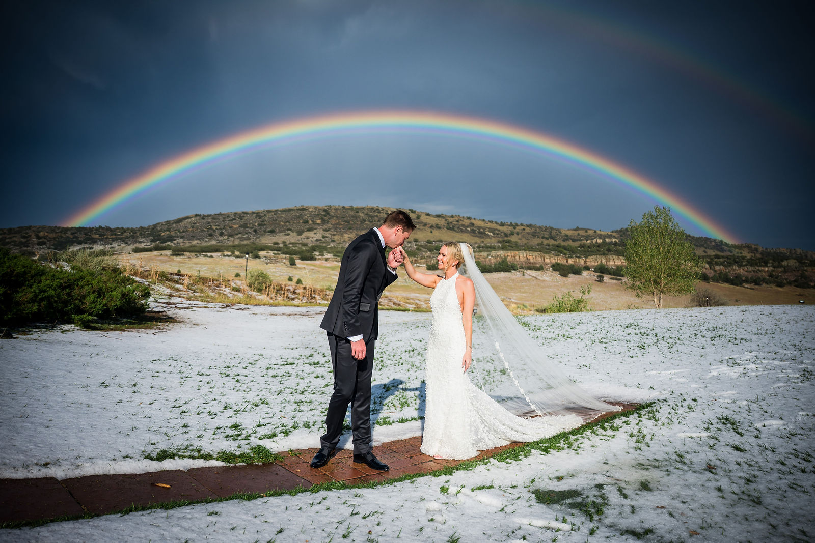 Bride and groom under a full rainbow on the hail covered grounds at The Manor House