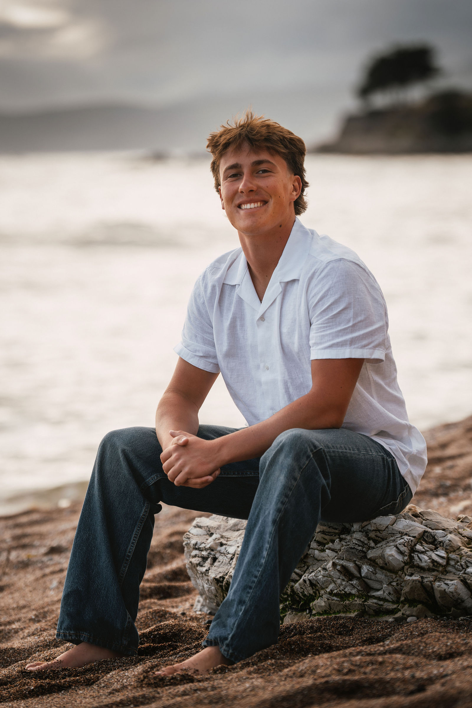 Senior boy sitting on coastal rocks, relaxed and confident