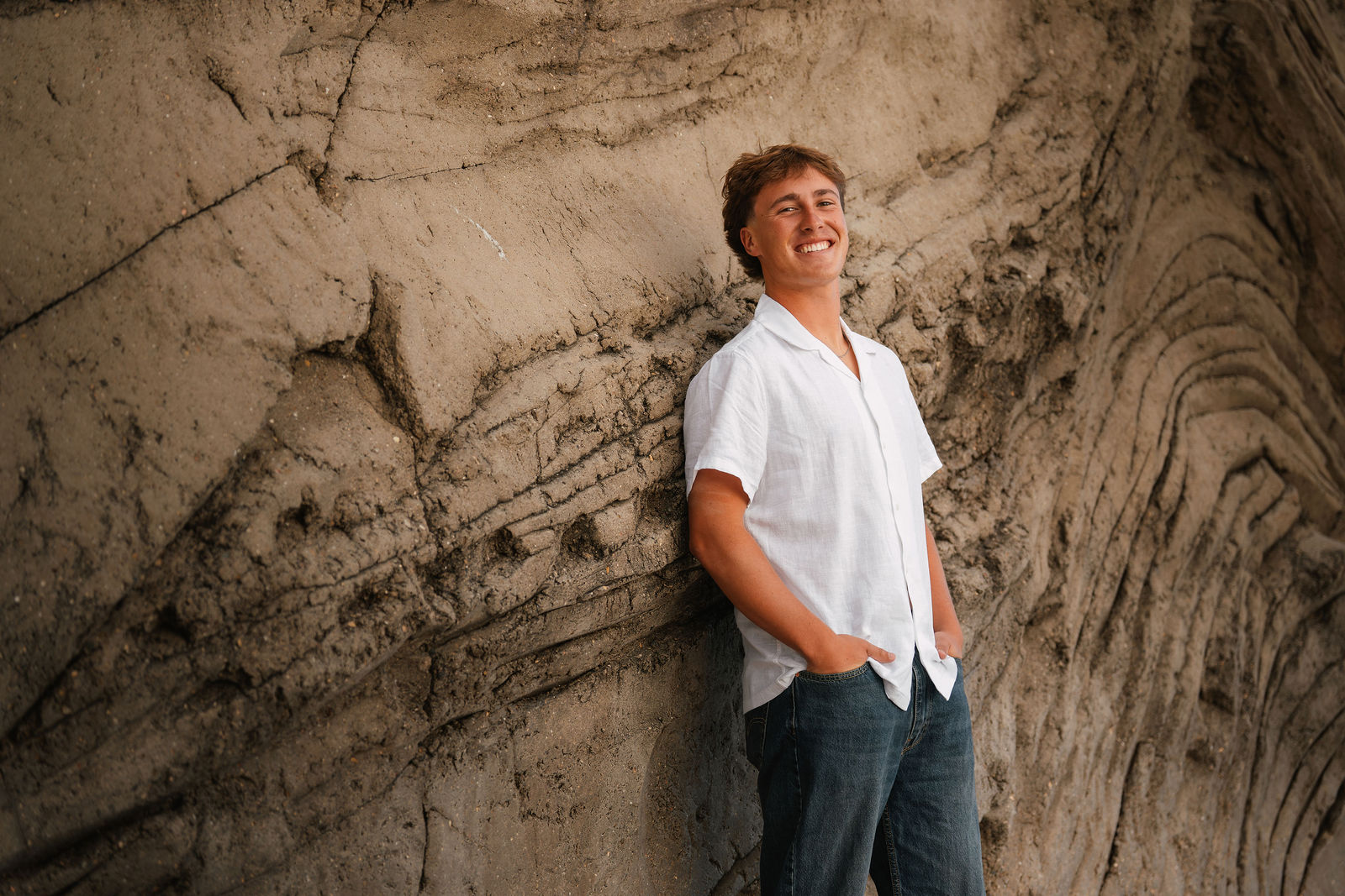 Senior boy leaning against sandstone wall, relaxed smile