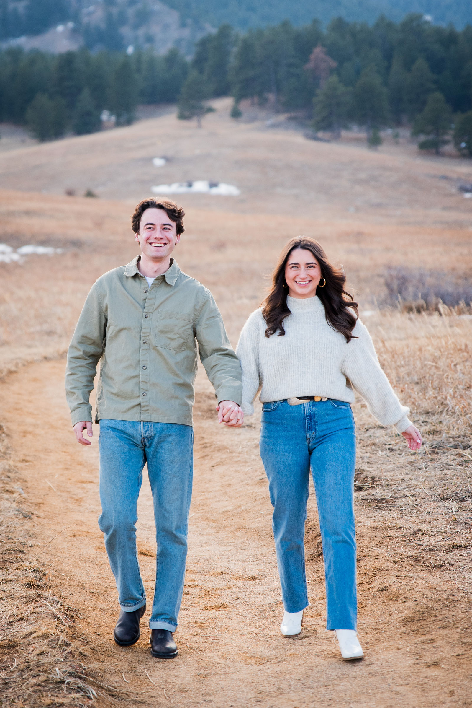Couple in an olive shirt jacket and a cream sweater with jeans in golden Colorado grass at Chautauqua
