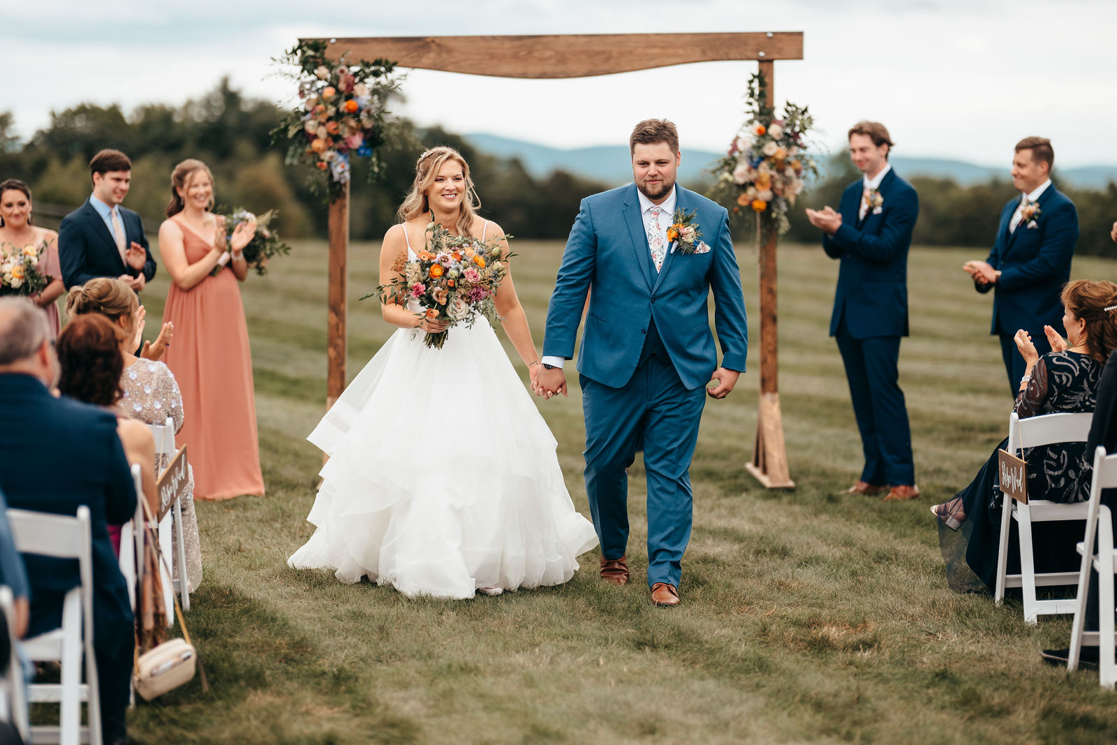 Newlyweds recessing hand in hand from the floral wooden ceremony arbor with mountains in the distance at Dell-Lea