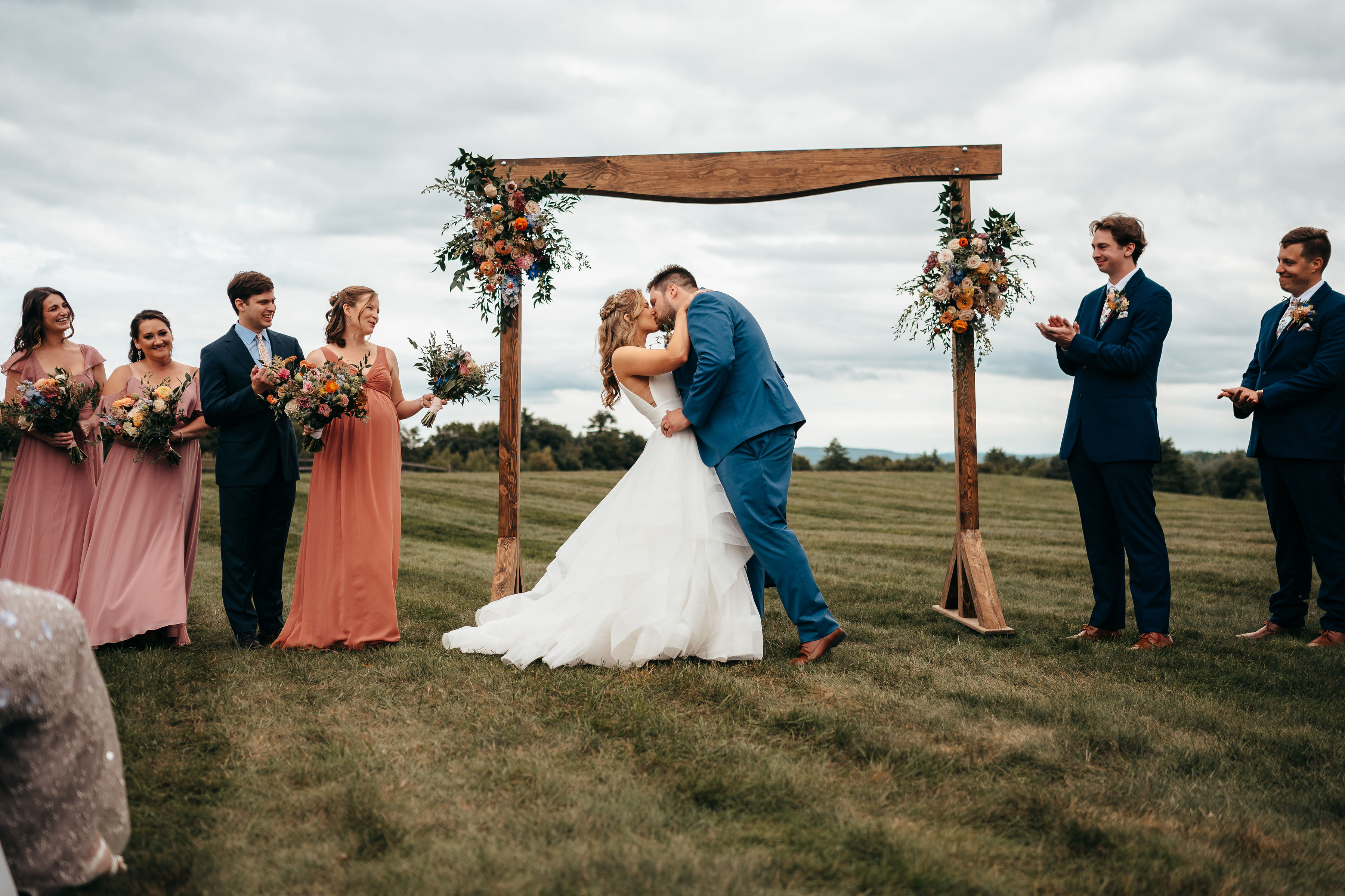Ceremony kiss under the wooden floral arbor with mountain views at Dell-Lea in Chichester NH