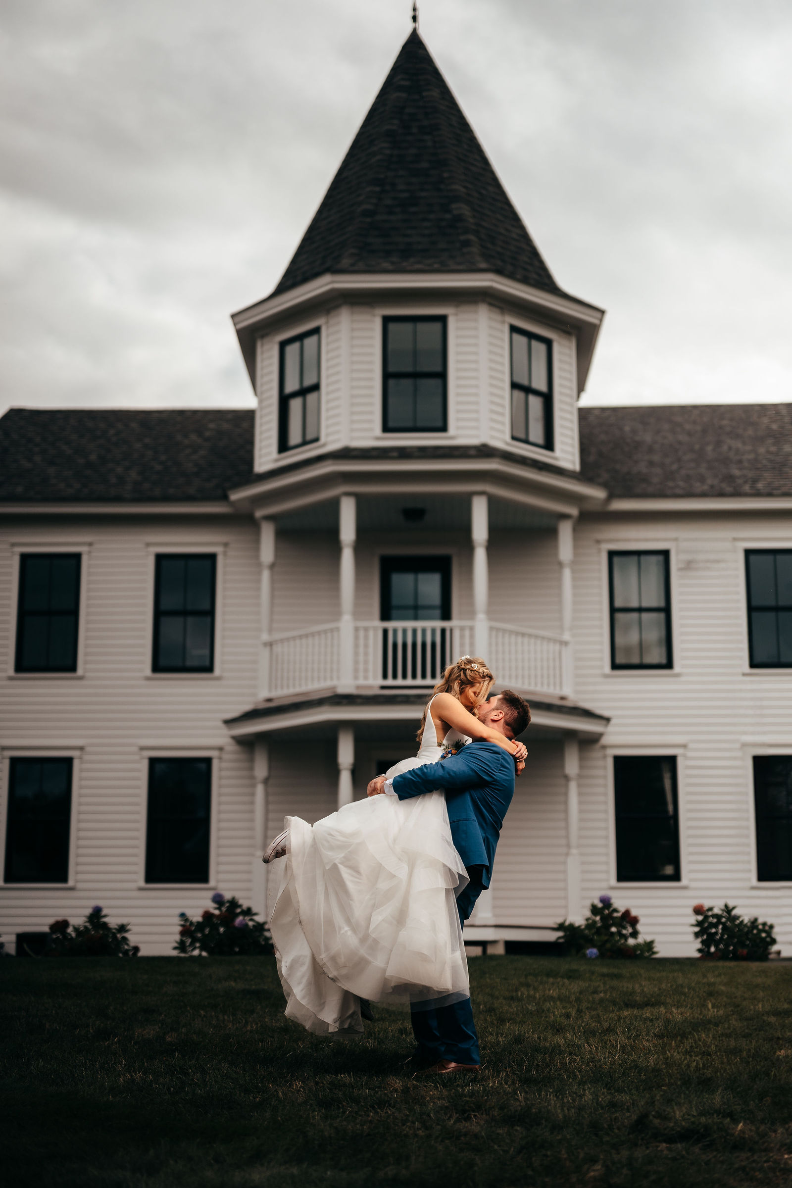 Groom lifting the bride for a kiss in front of the manor house at dusk at Dell-Lea