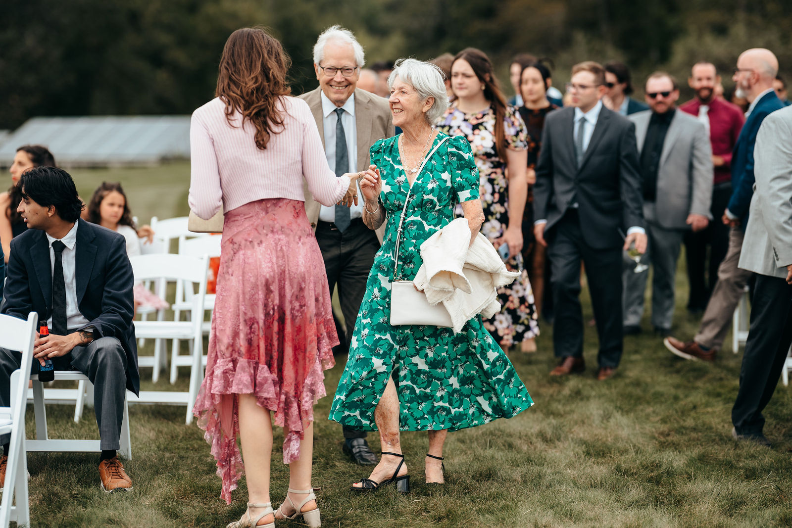Wedding guests mingling among white ceremony chairs on the lawn at Dell-Lea