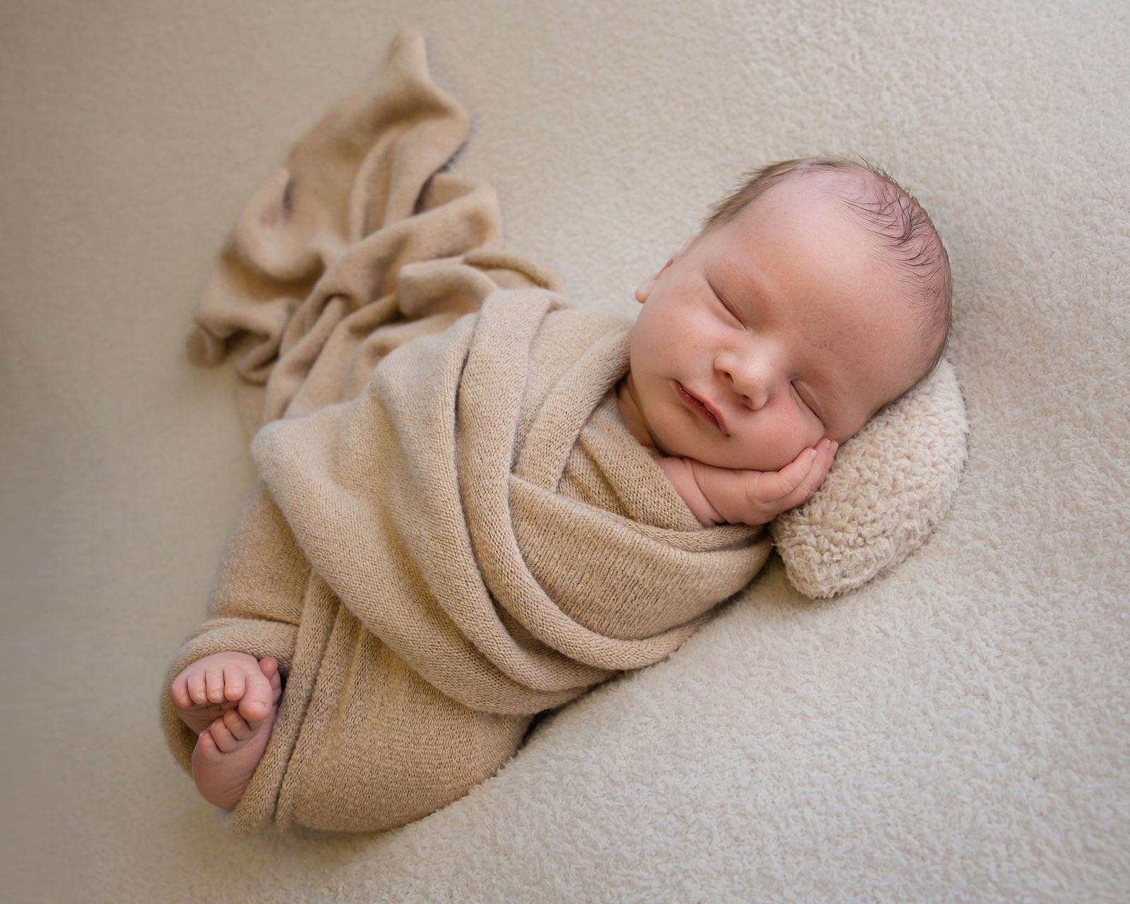 Sleeping newborn wrapped in neutral beige fabric on a soft cream backdrop