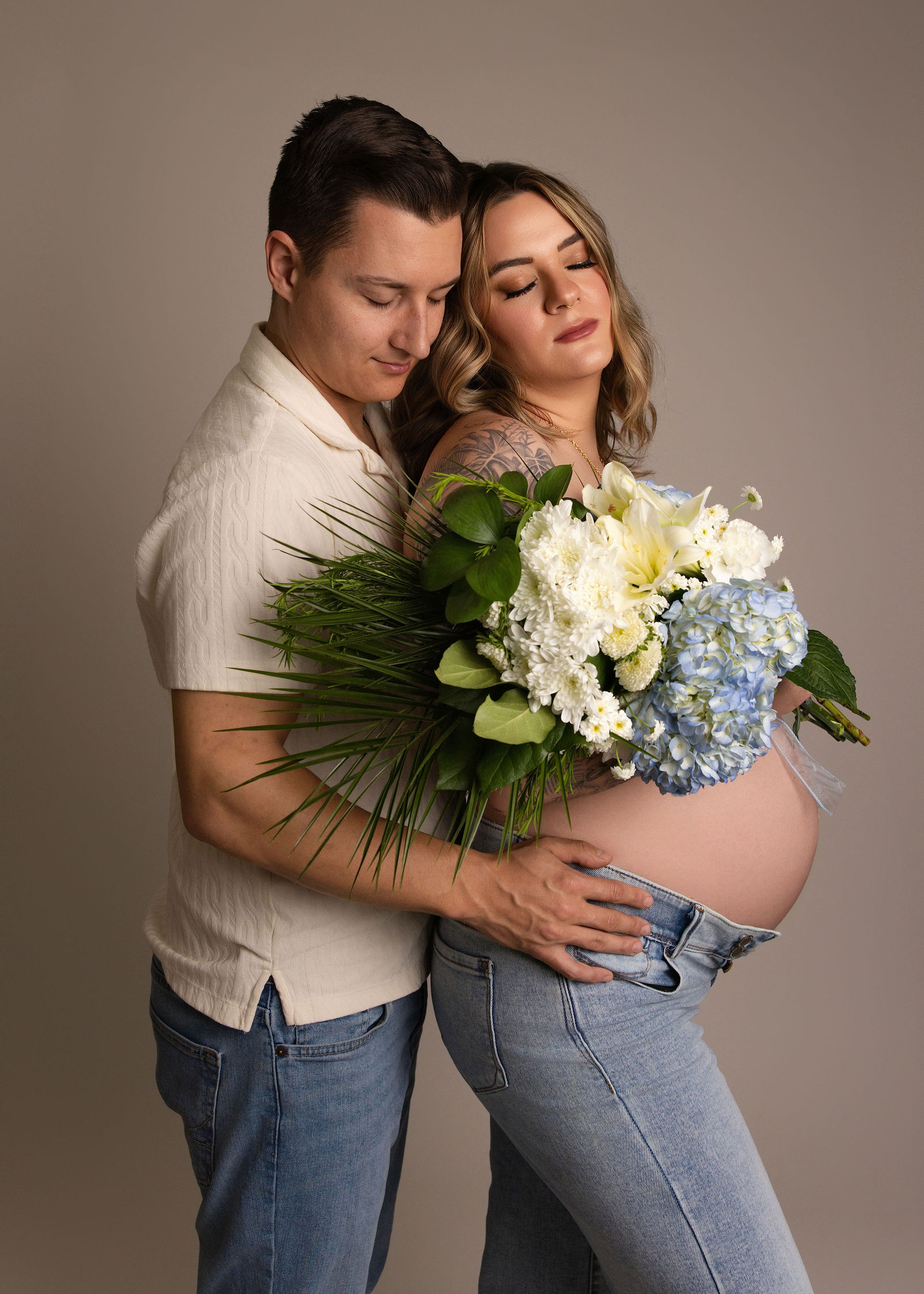 Expecting couple posed together in the studio with flowers during a maternity photography session