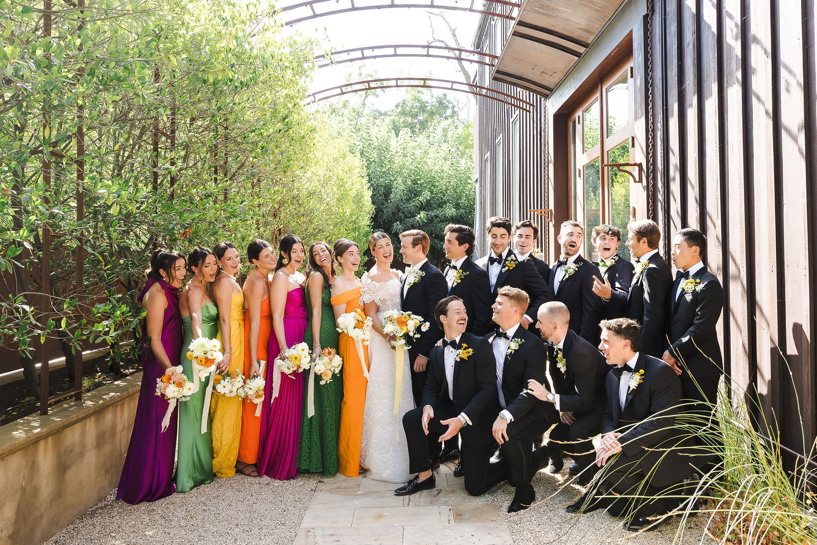 Full wedding party in jewel tone dresses and black tuxedos under the arbor at a Barndiva wedding in Healdsburg California