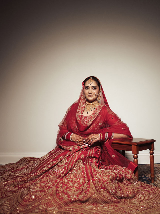 Avneet seated in her embroidered red bridal outfit, with the skirt arranged around her