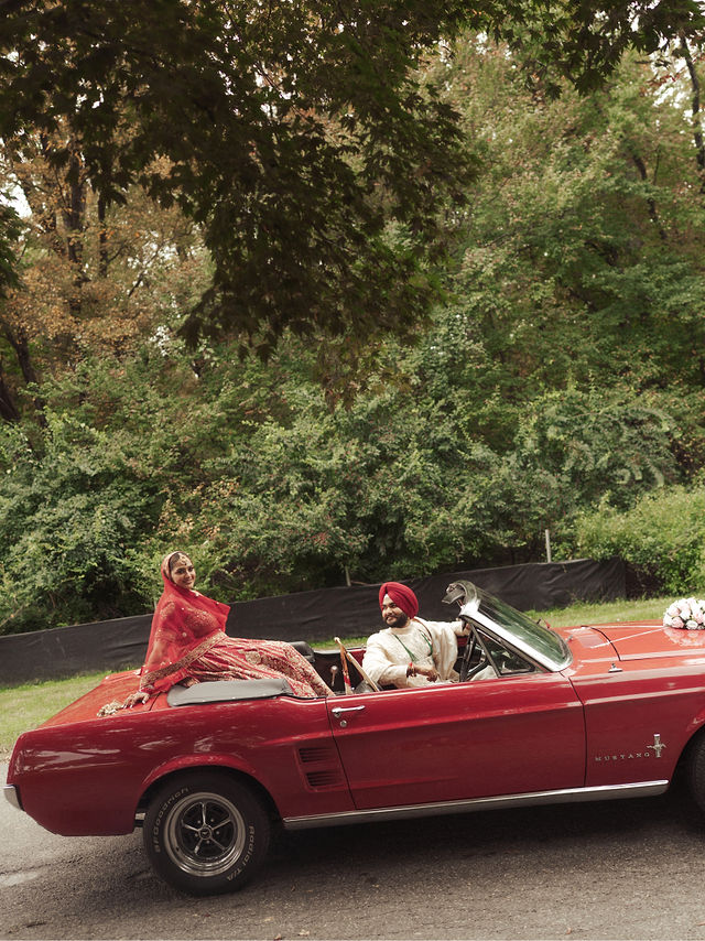 Avneet and Sarvan in a red open-top car beside green trees
