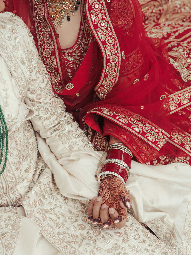 Avneet and Sarvan holding hands, with red bridal bangles and embroidered wedding attire