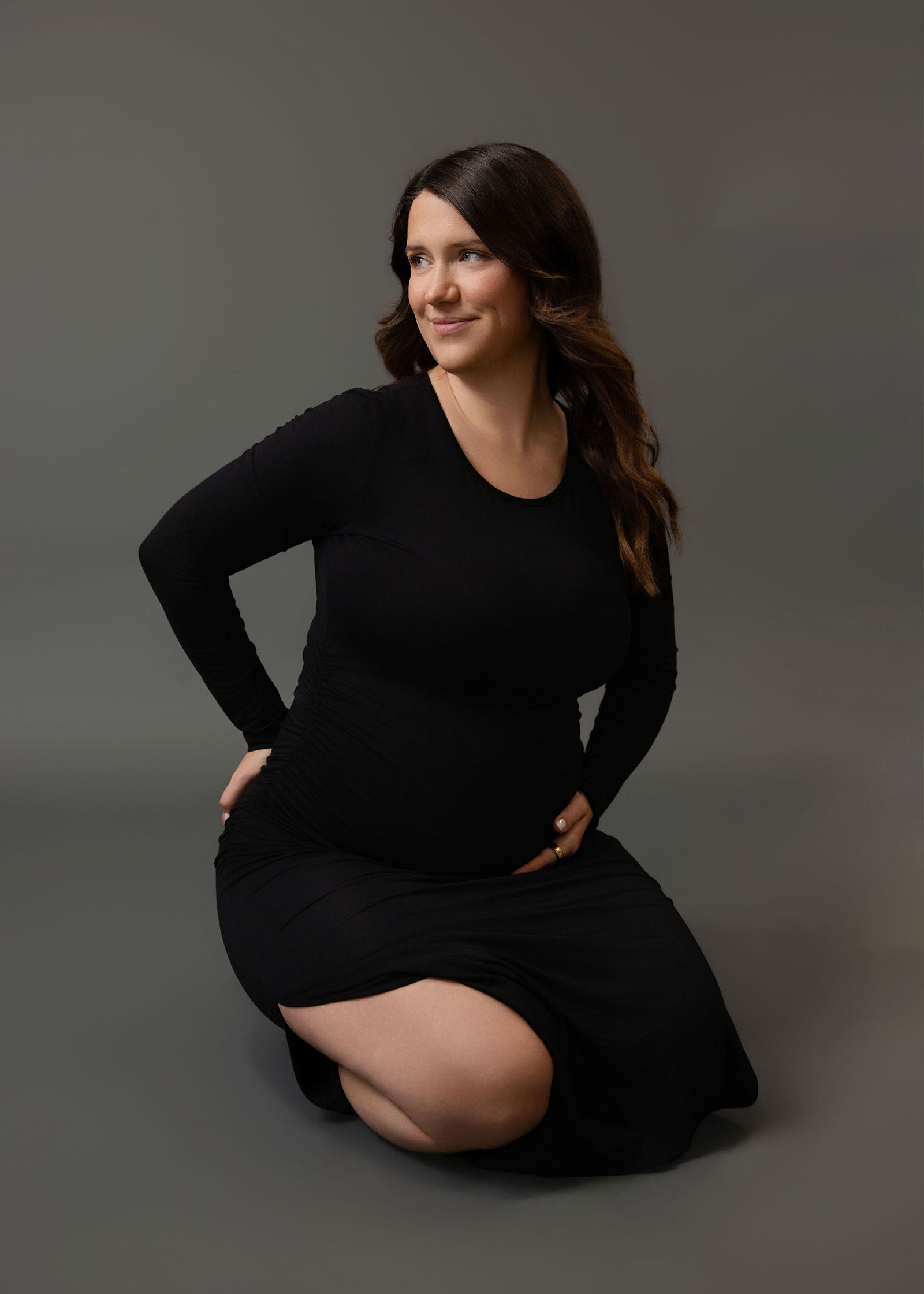 Pregnant woman kneeling in a long black dress for an elegant studio maternity portrait