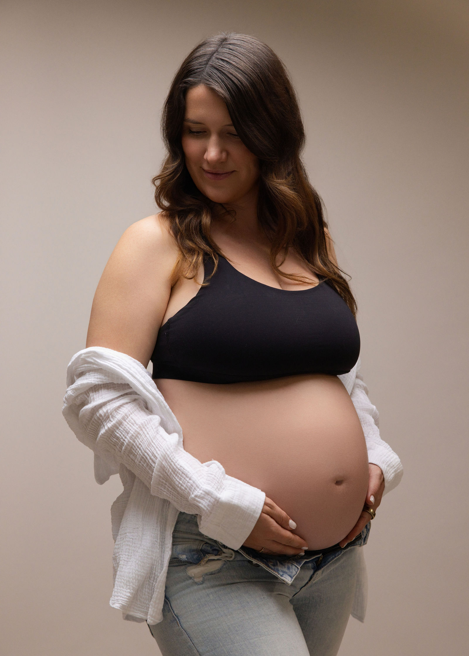 Pregnant woman in jeans and a black top posed in soft neutral studio lighting