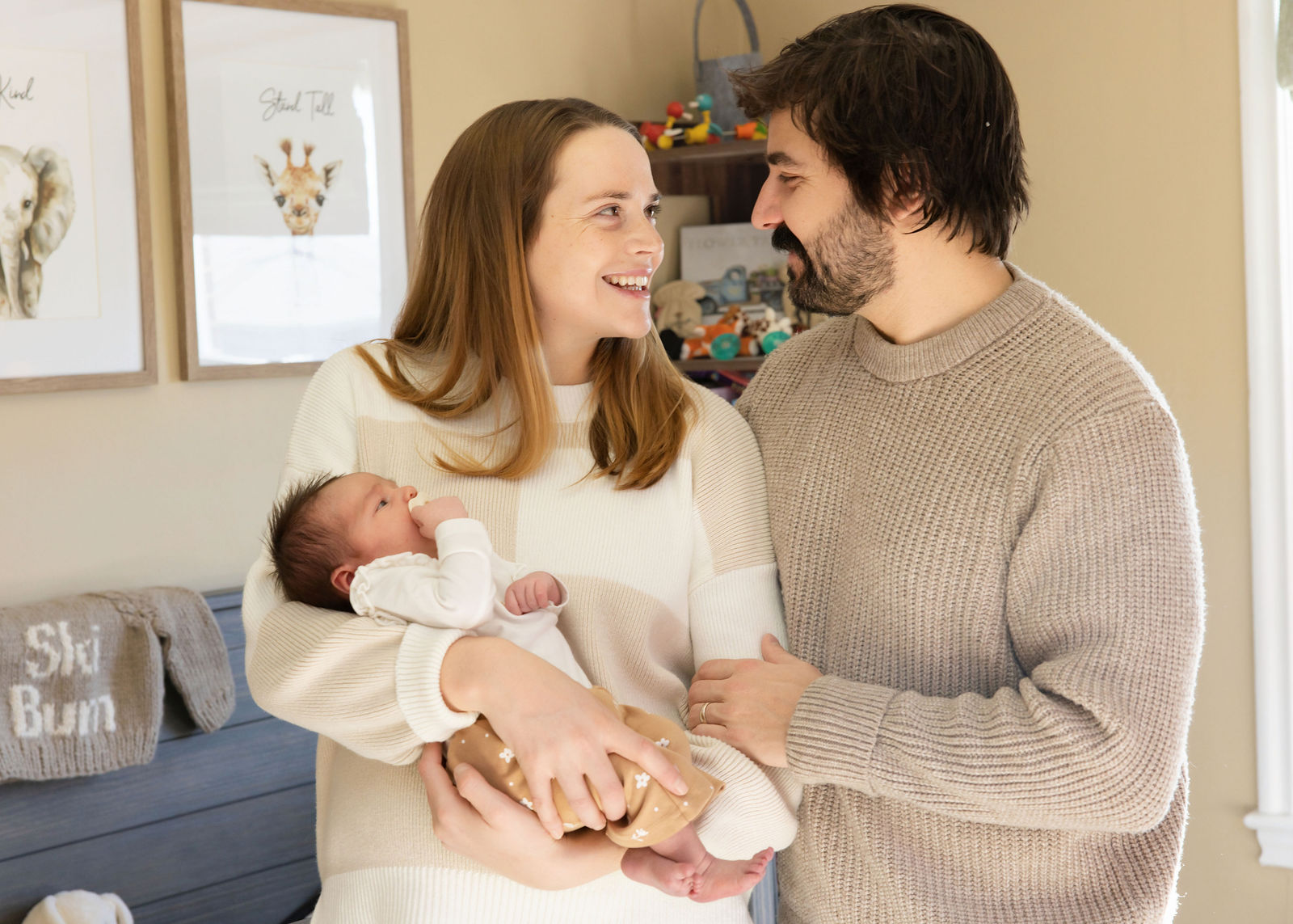 Mother and father smiling at each other while holding their newborn baby in the nursery
