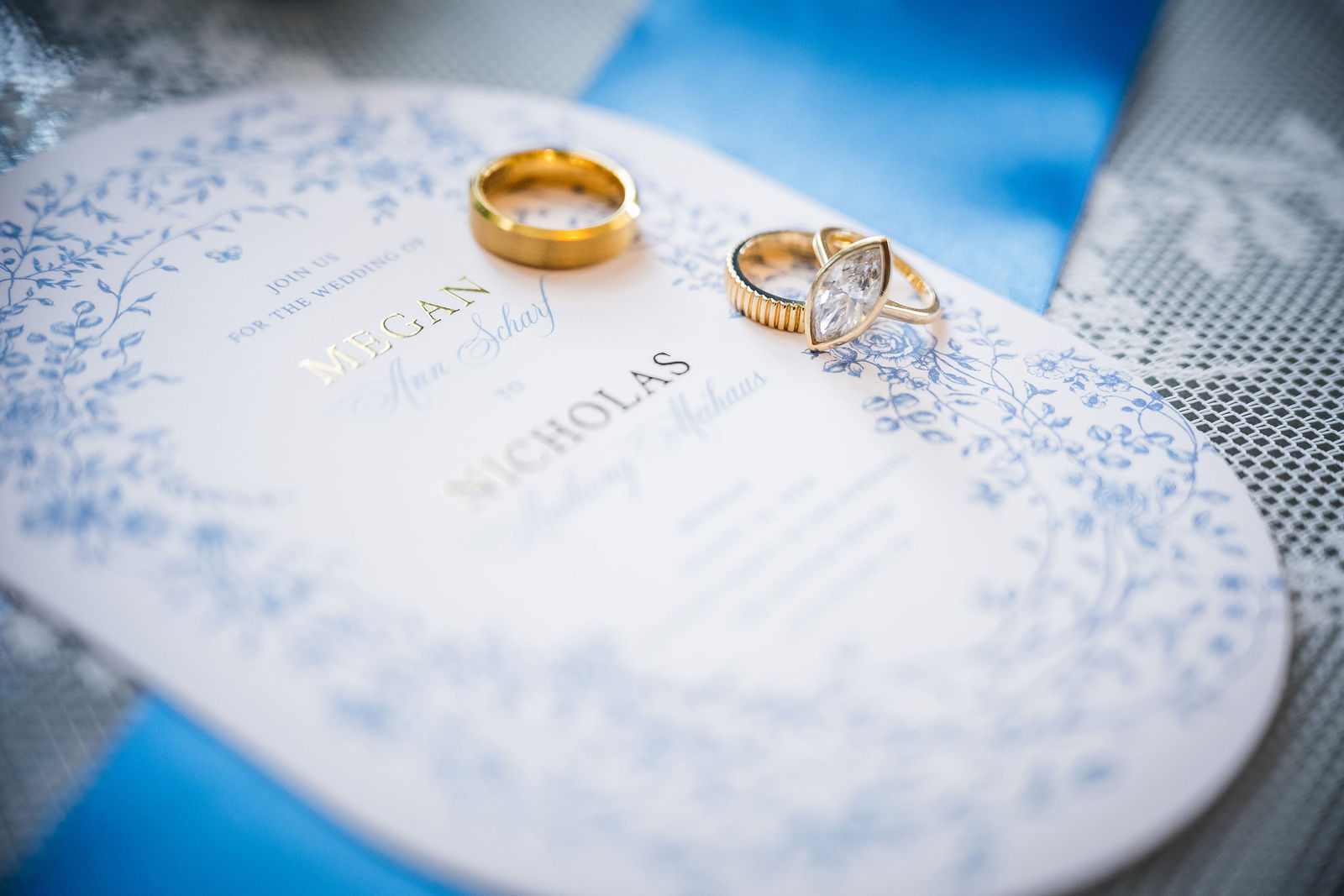 Wedding bands resting on a dusty blue oval invitation before a Littleton Colorado wedding