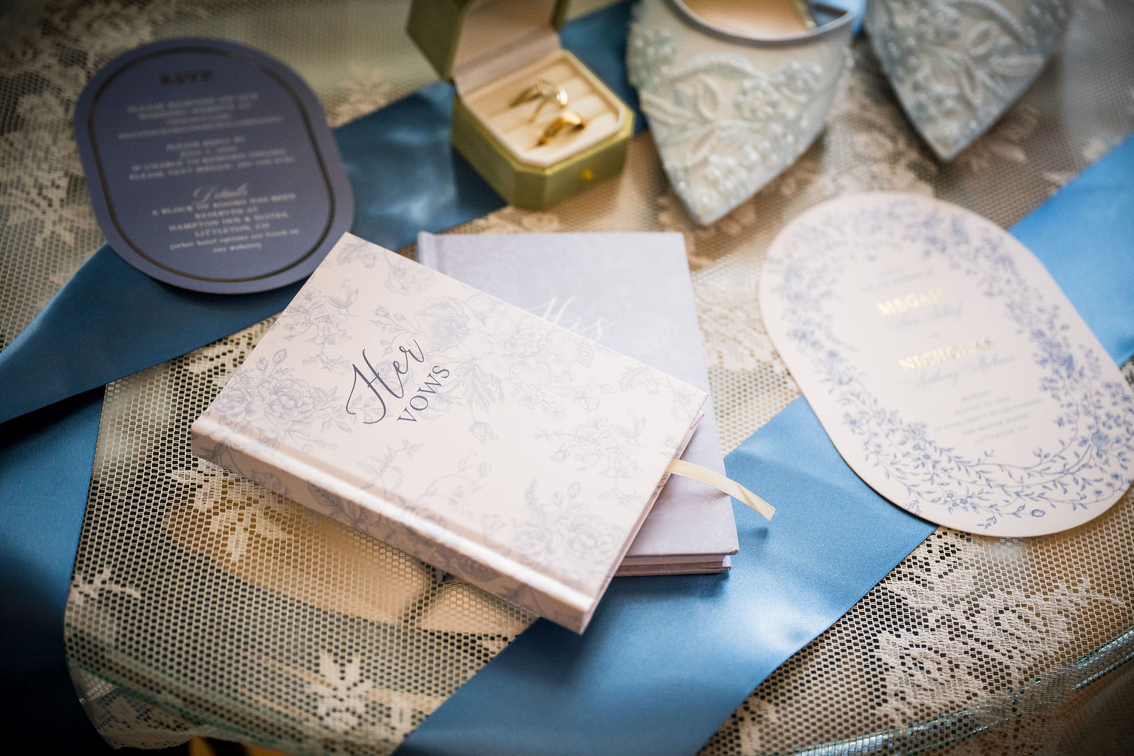 Vow books and the wedding invitation suite laid out on a dusty blue background