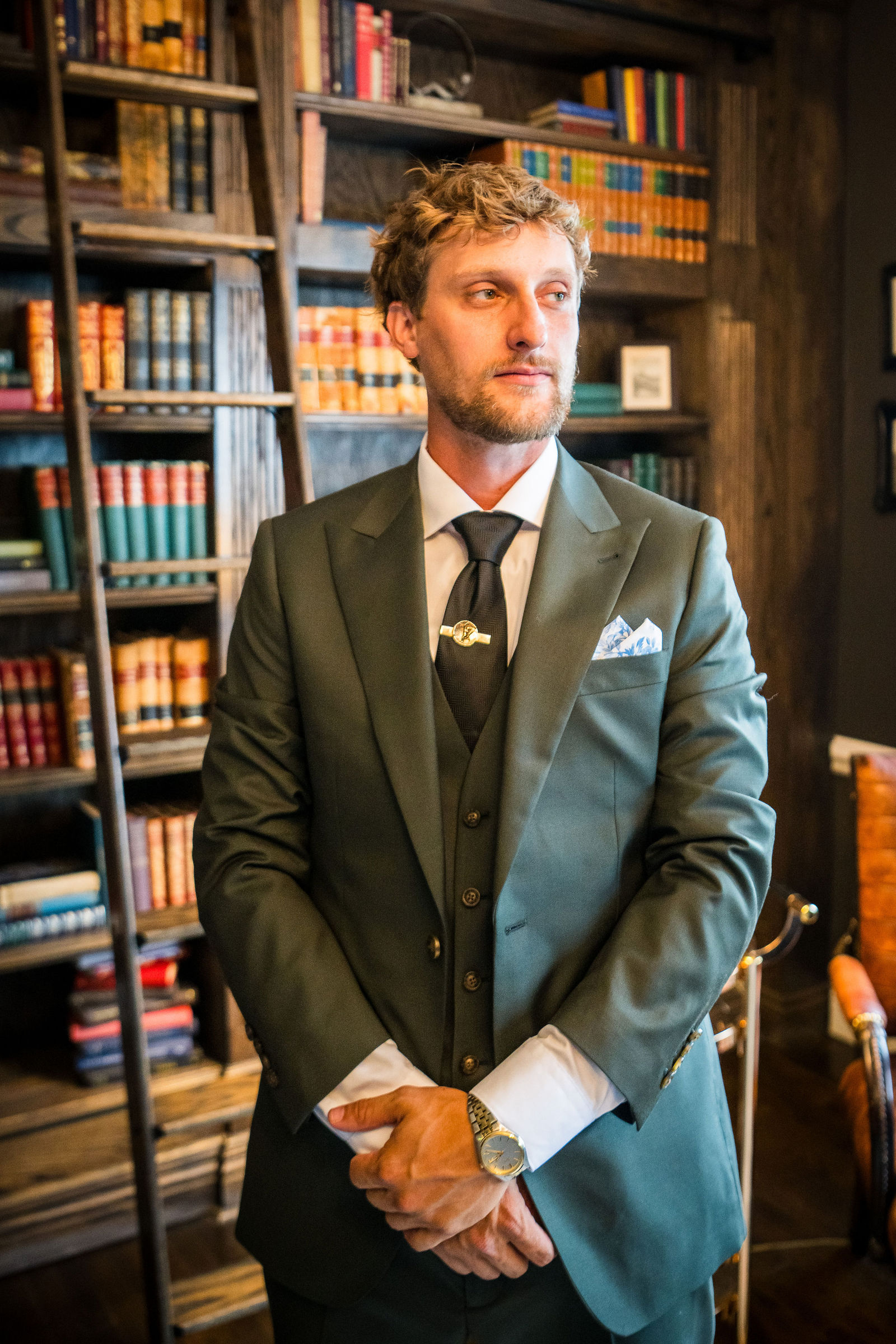 Groom in an olive green suit in the library at the Manor House