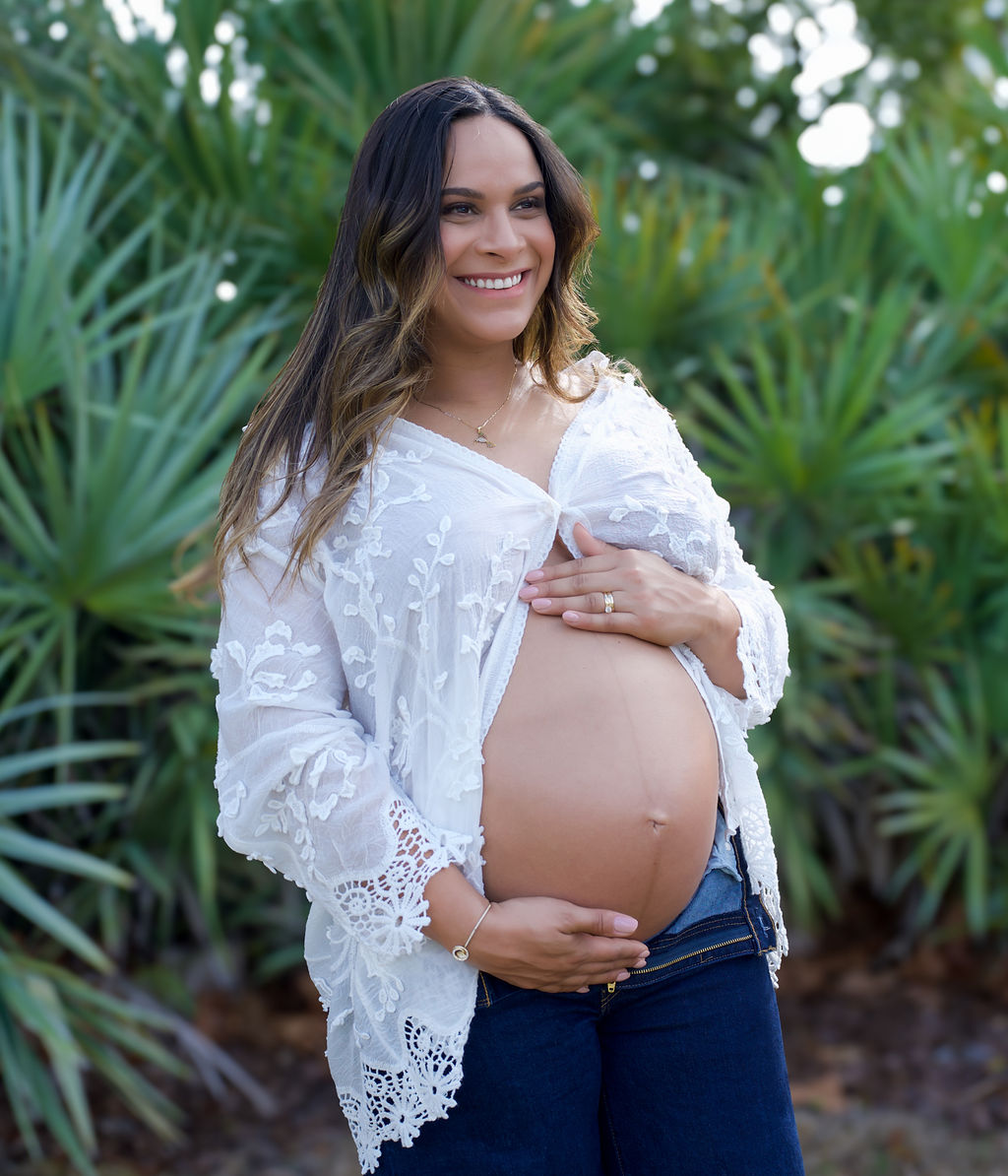 Mother-to-be in white lace and denim posed against lush greenery