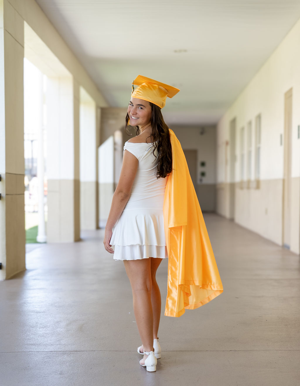 Graduate in a gold gown turning as she walks through a modern corridor