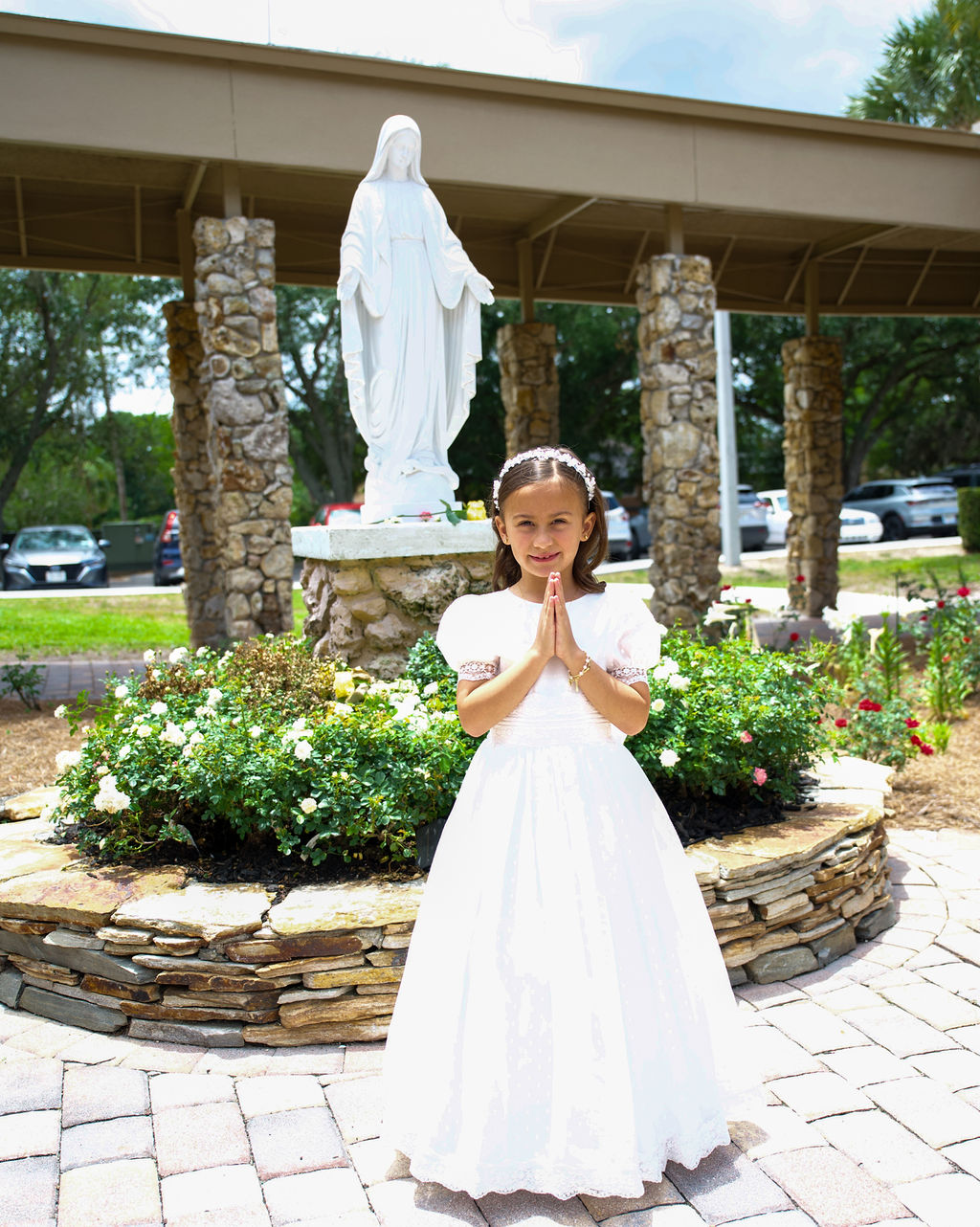 Child in a white communion dress posing in a peaceful garden