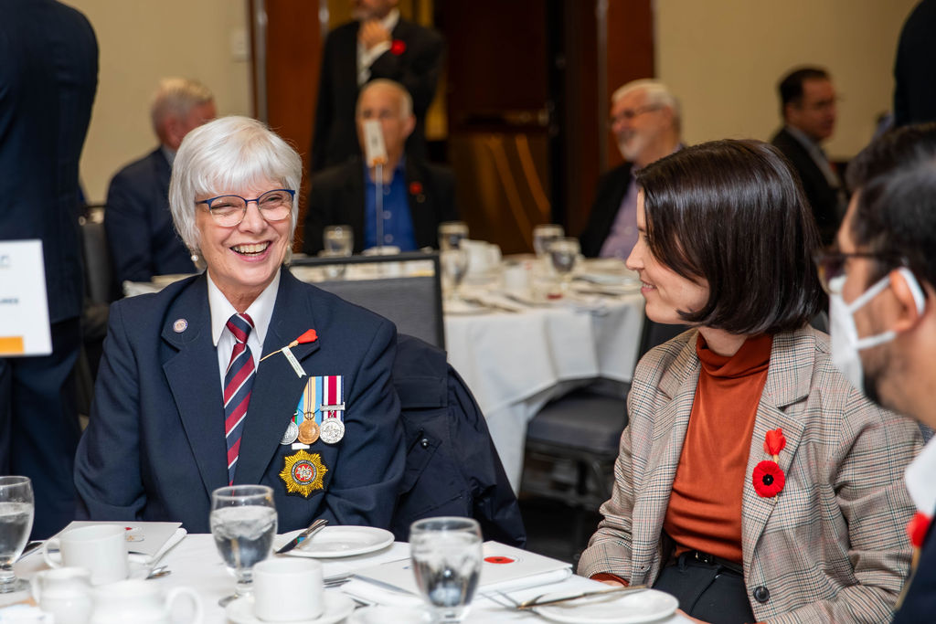 A veteran wearing her medals, smiling at her table at the Veterans' Tribute Lunch in Ottawa