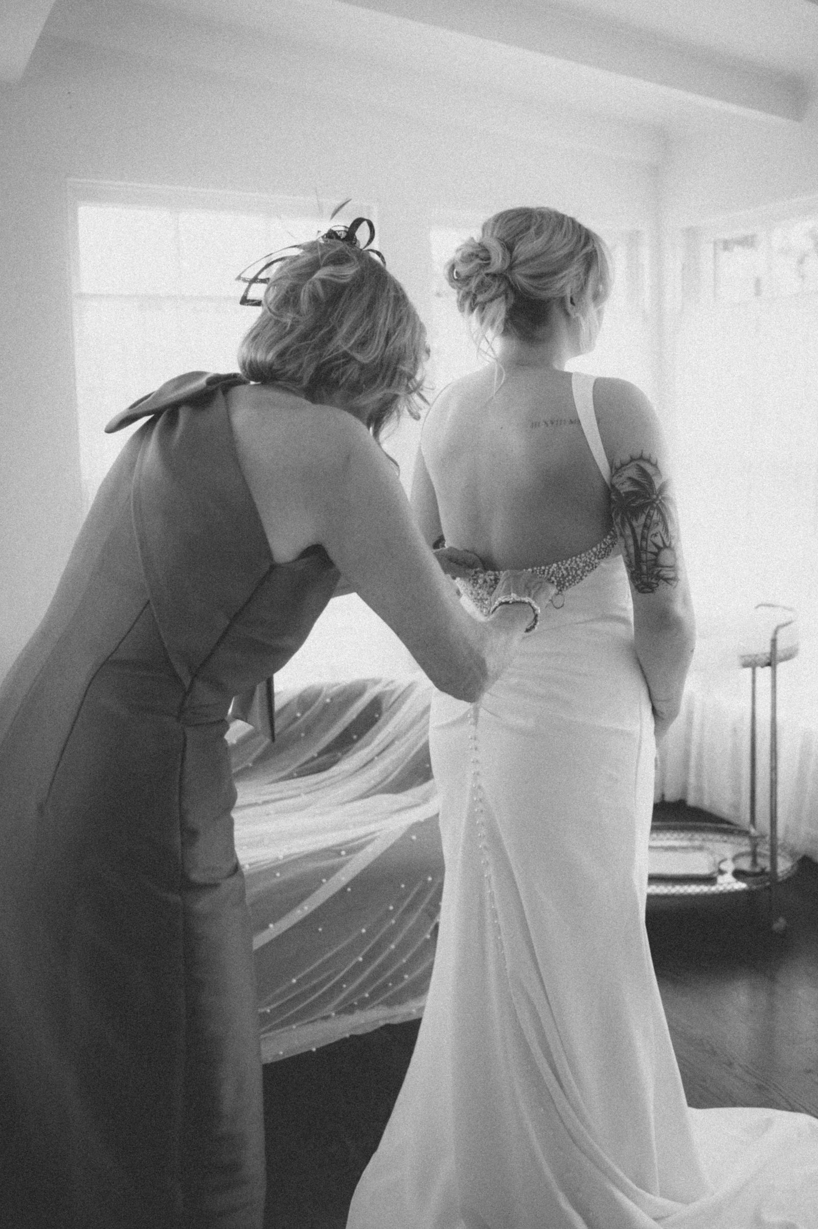 Bridesmaids fastening the back of the wedding gown in warm sepia tone