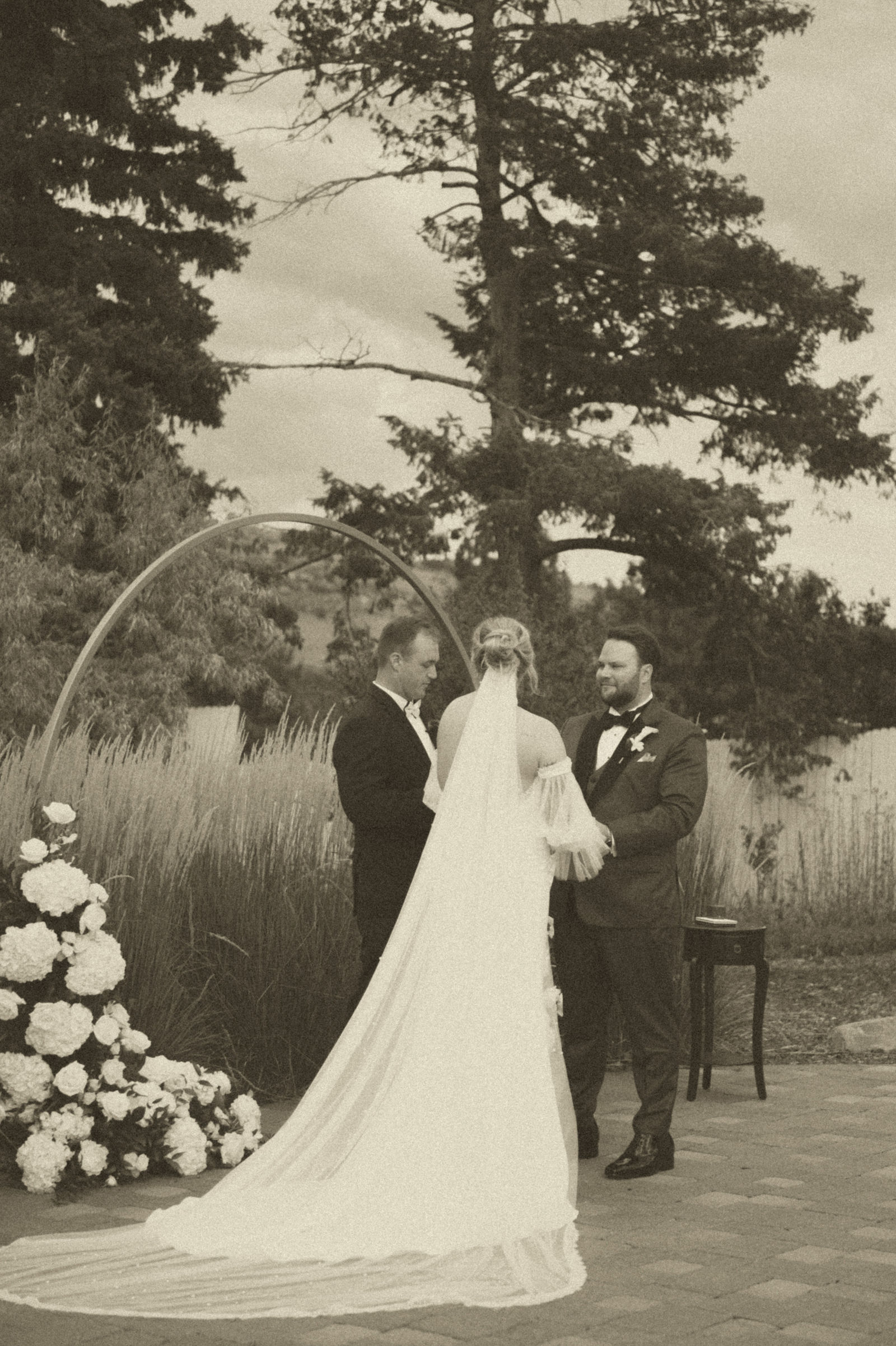 Bride and groom holding hands at the ceremony arch in sepia tone