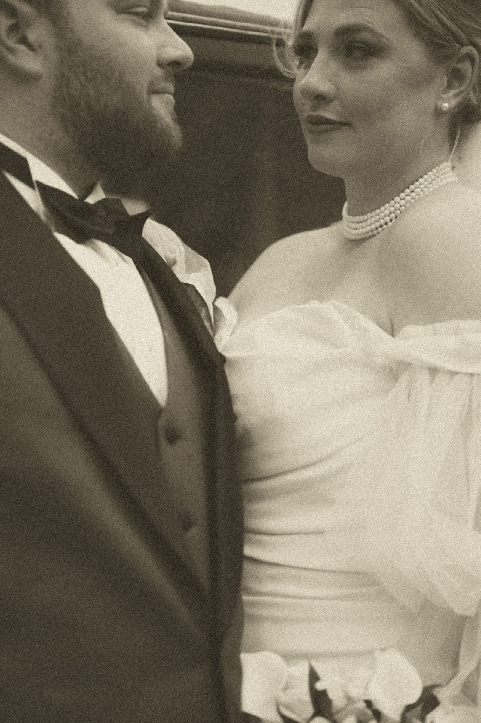 Bride posing beside an antique car in her gown and veil