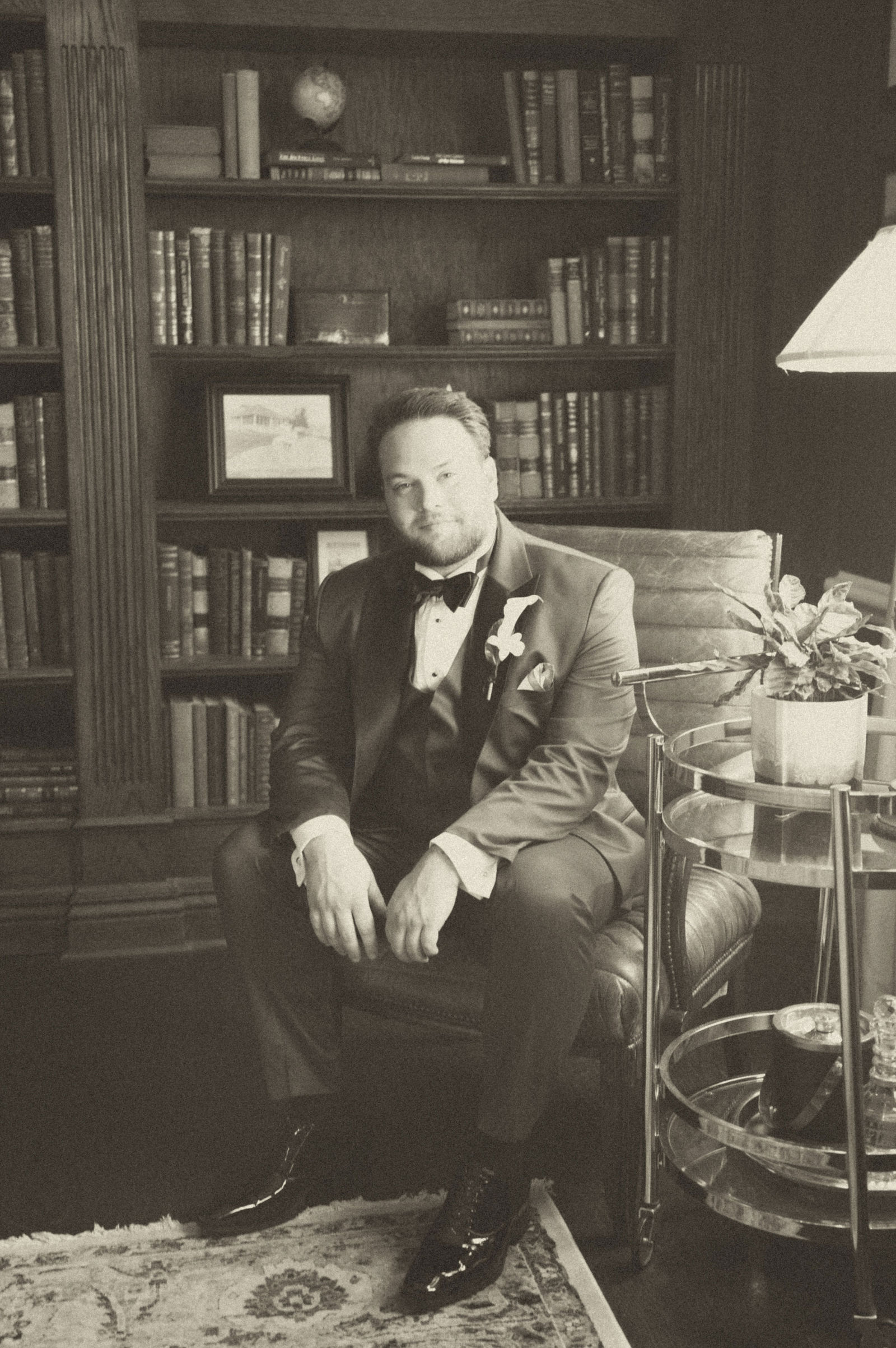 Groom seated in the library at The Manor House in a vintage film tone