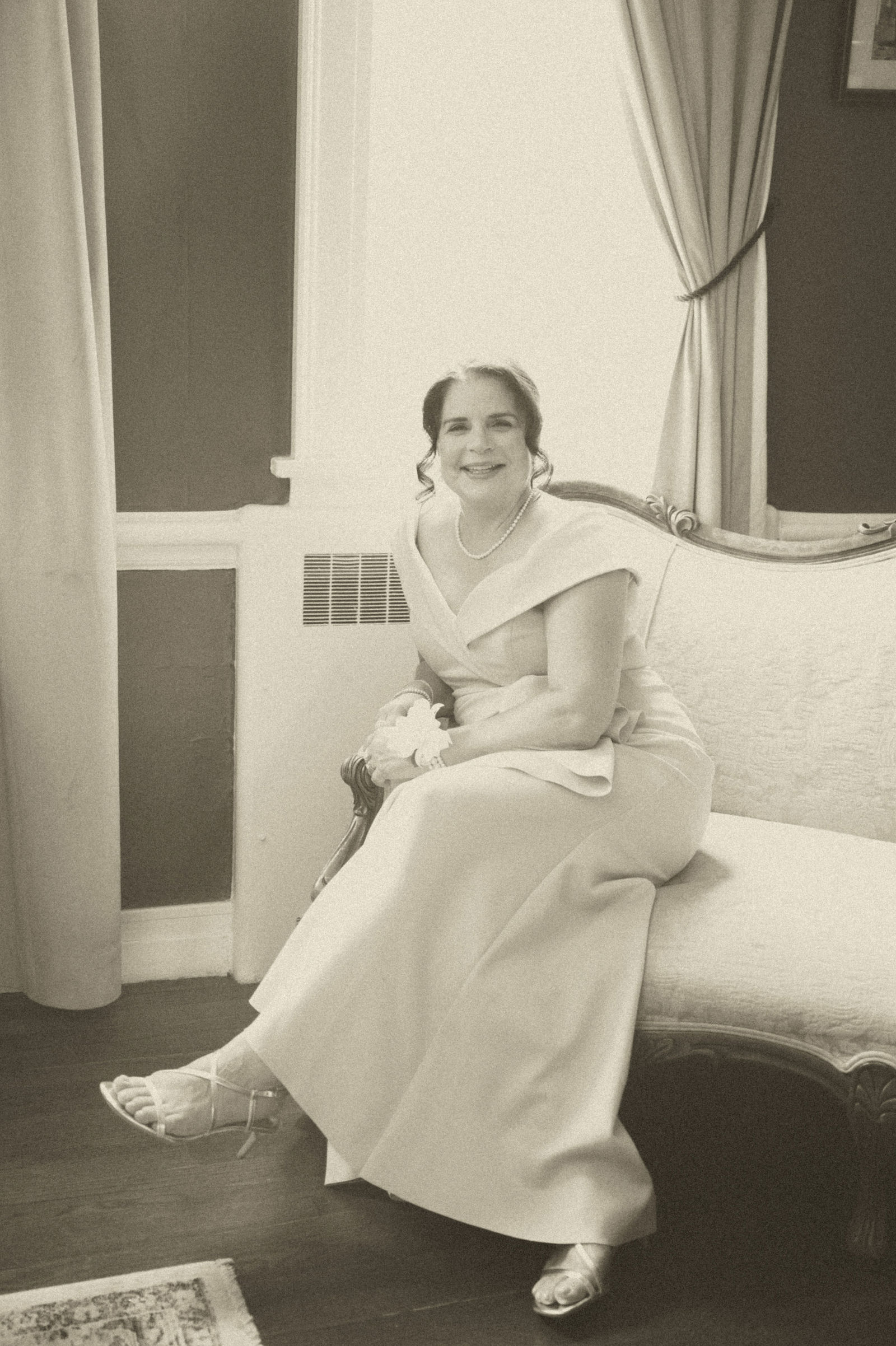 Bride standing at a bright window in her gown edited in vintage sepia