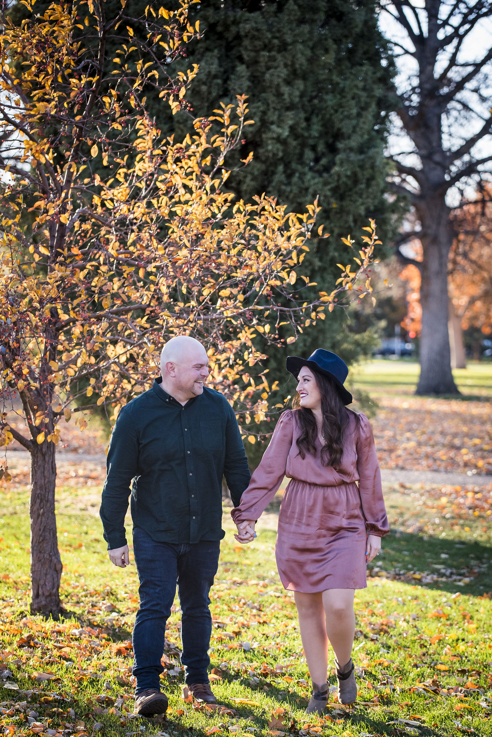 Couple in a dusty mauve dress and navy felt hat beside a black button down among fallen autumn leaves