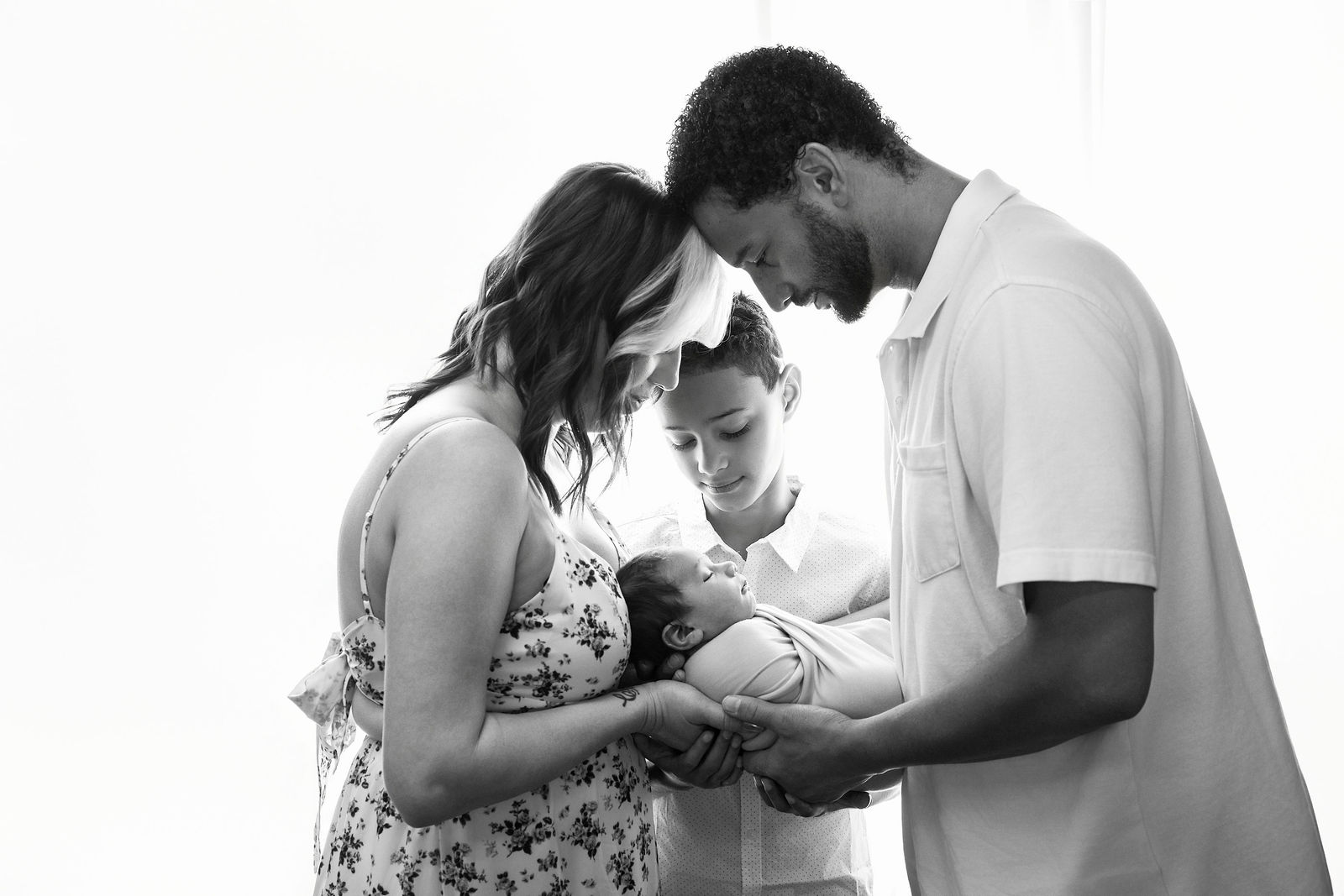 Parents and older sibling gathered around their newborn baby during a family newborn portrait