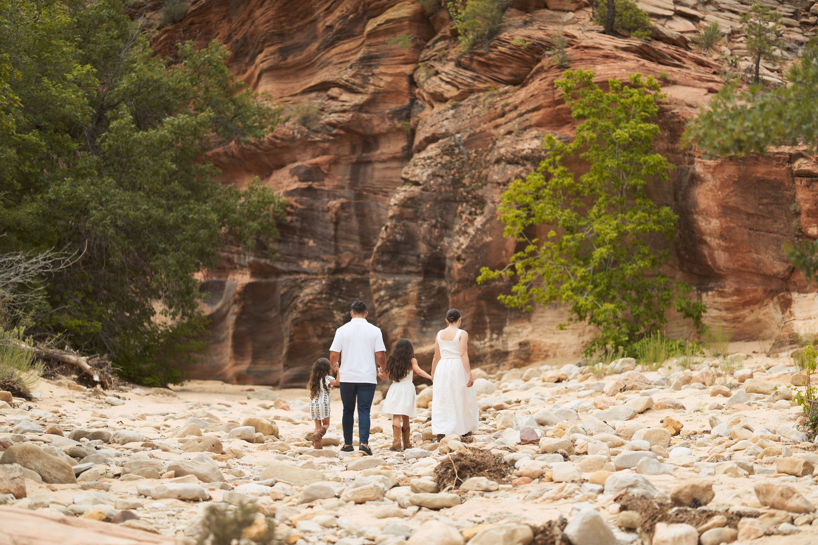 Family of four holding hands while walking across rocks in Southern Utah