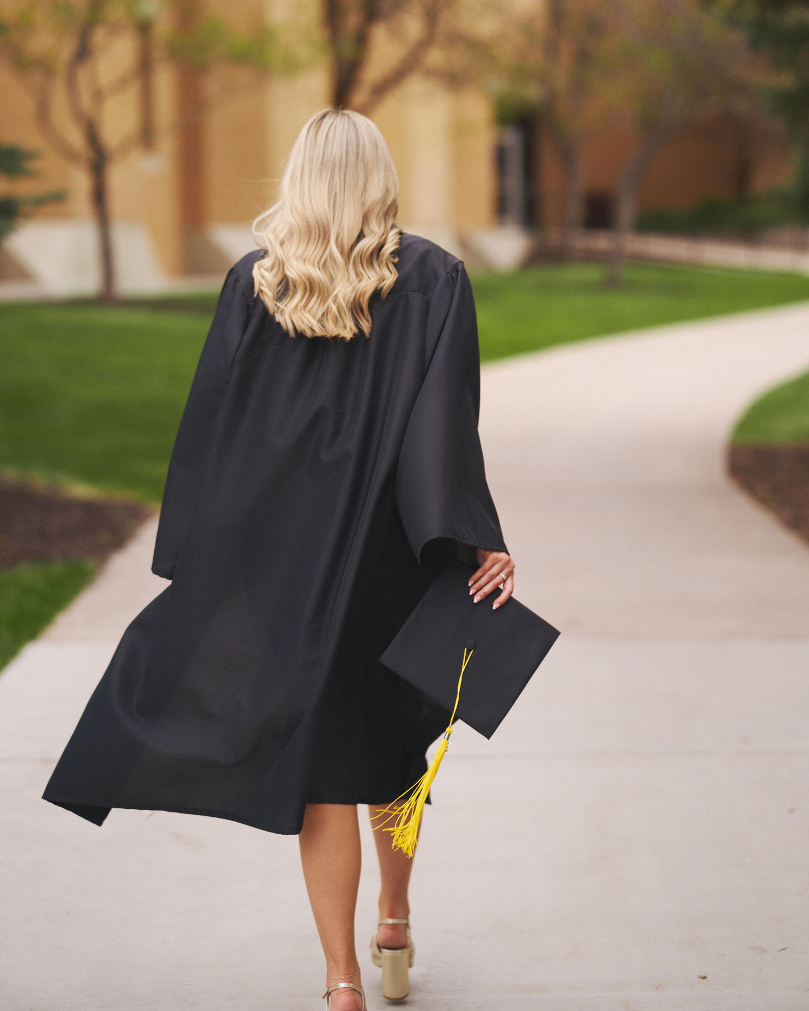 Graduate walking across campus with her gown flowing and cap in hand