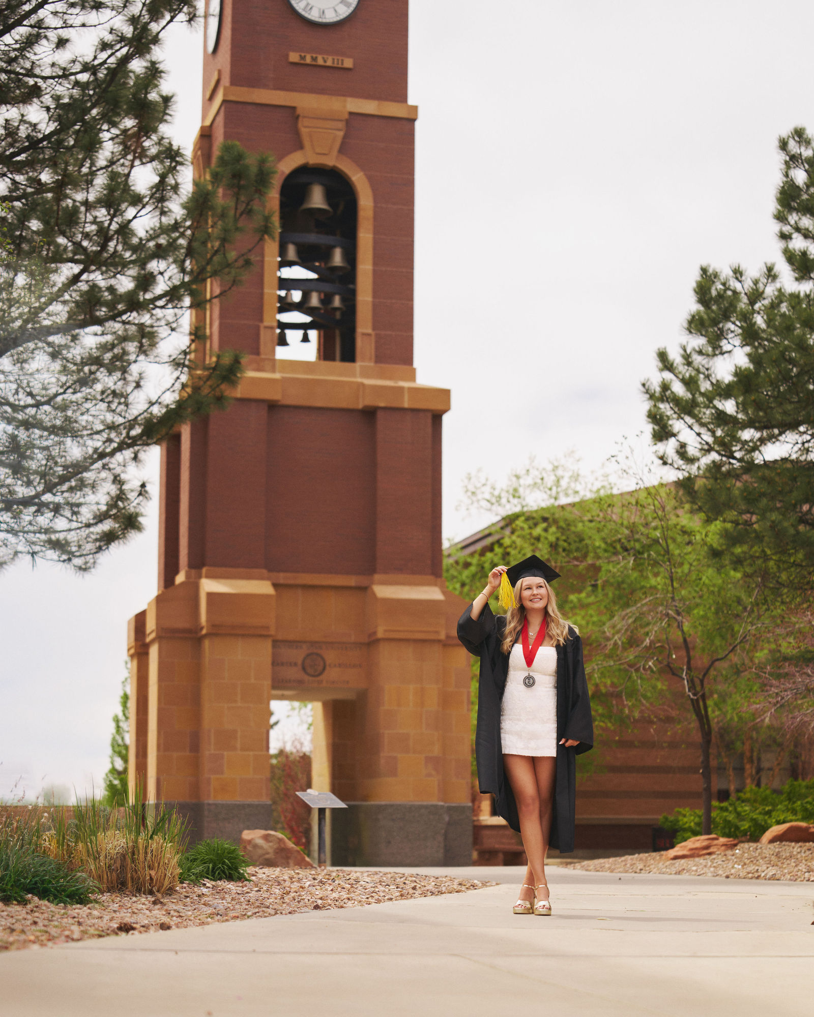 Full length graduation portrait in front of a college tower and campus