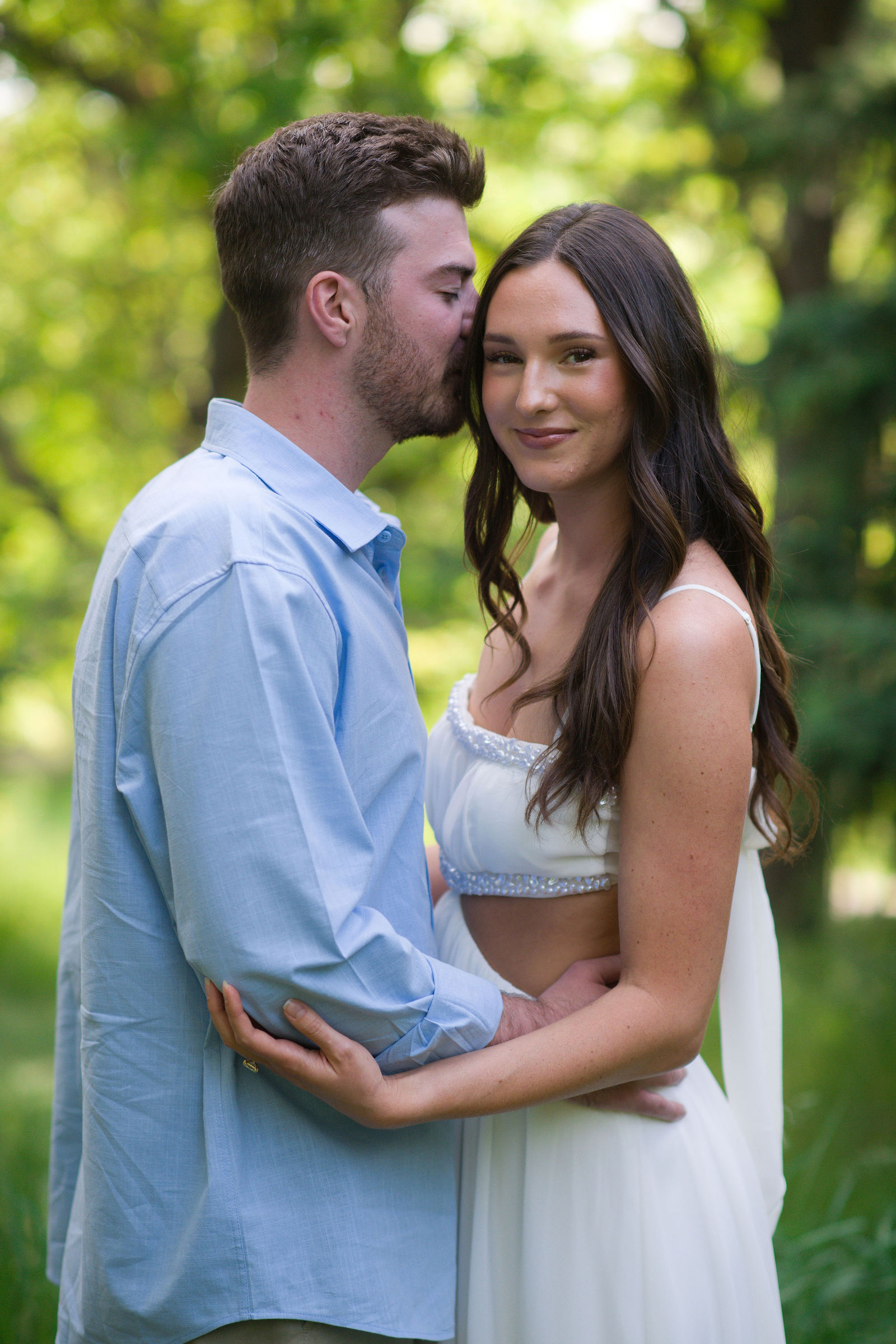 Engaged couple embracing beneath the trees