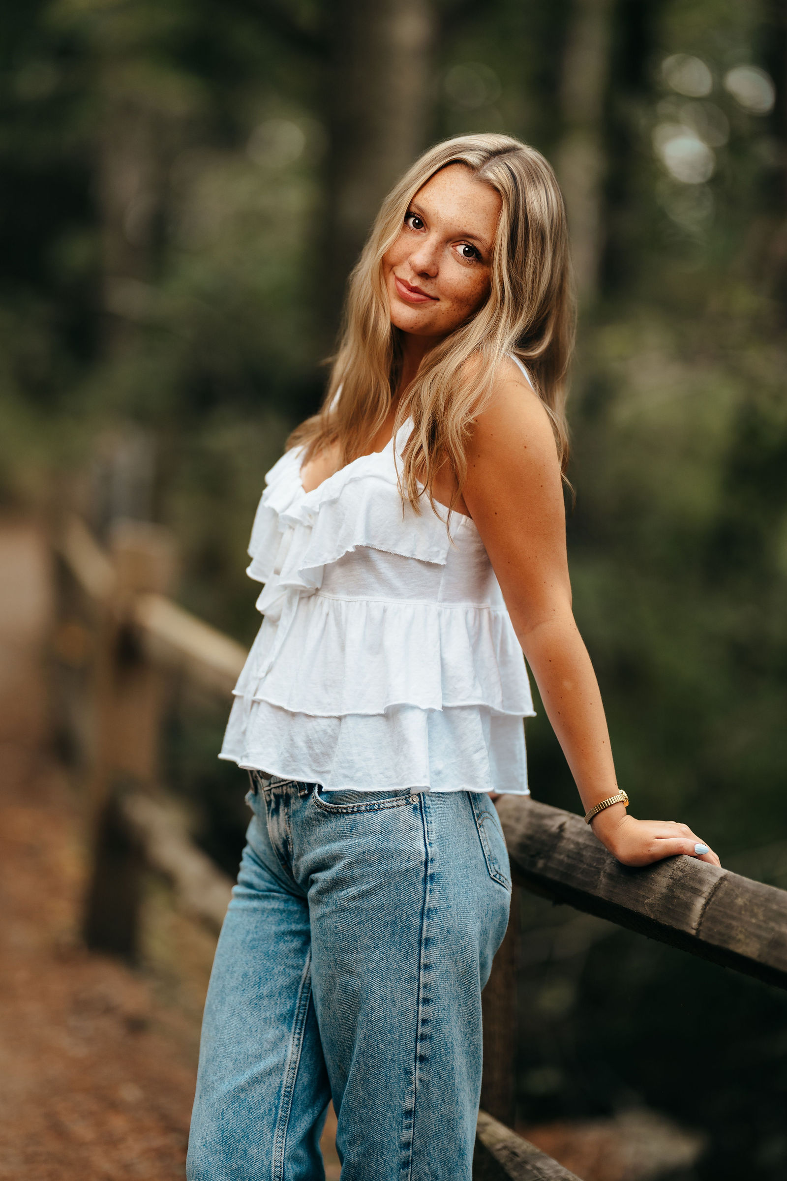 Syd leaning on a wooden rail in the woods during her senior portrait session