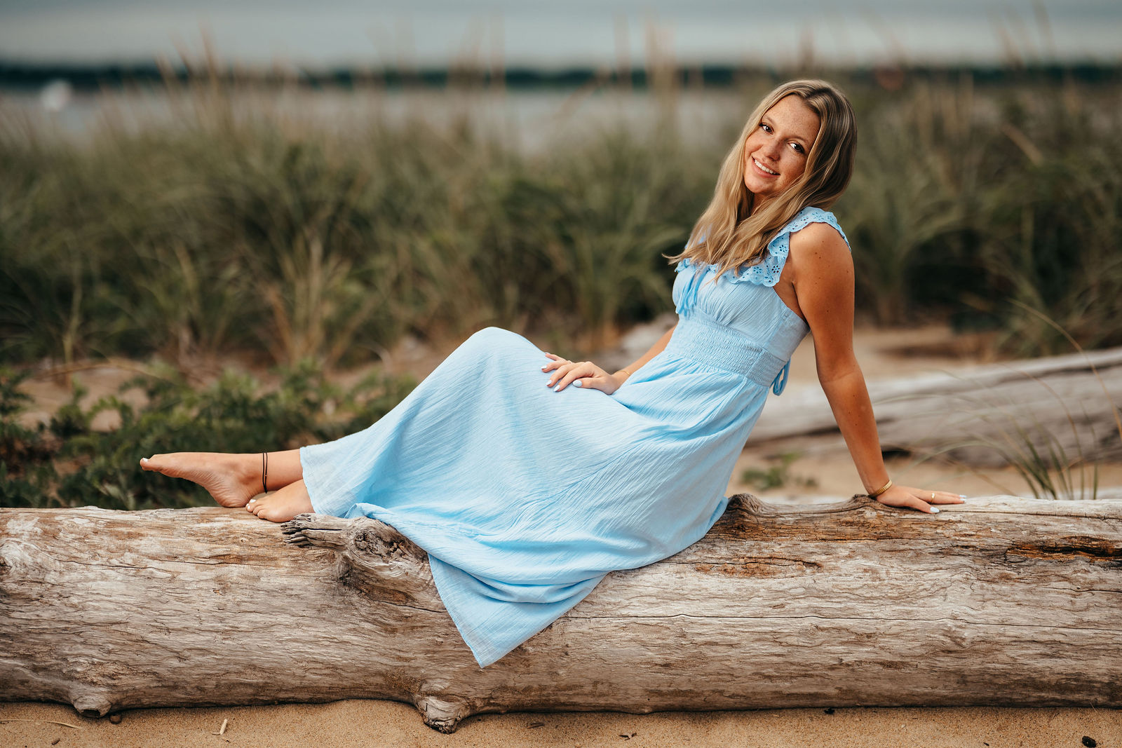 Syd lying on driftwood in a blue dress at the beach during her senior portrait session