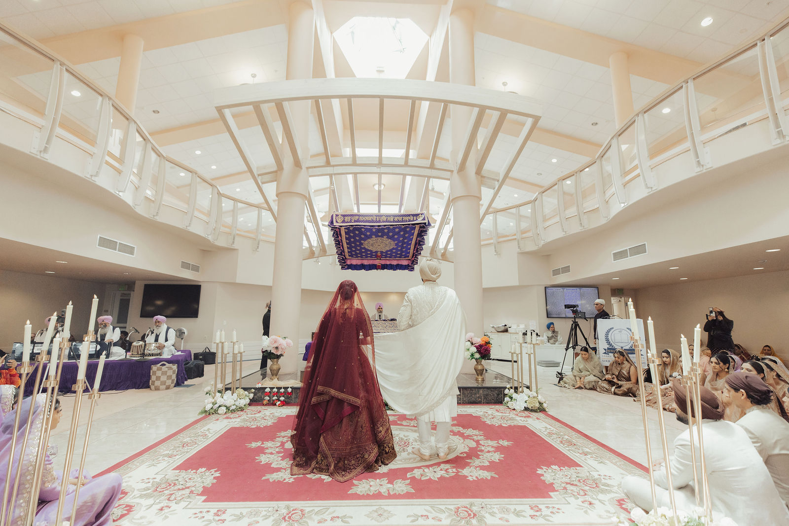 Kira and Harry during their Anand Karaj beneath the skylit ceiling and white balconies of Sikh Institute Fresno.